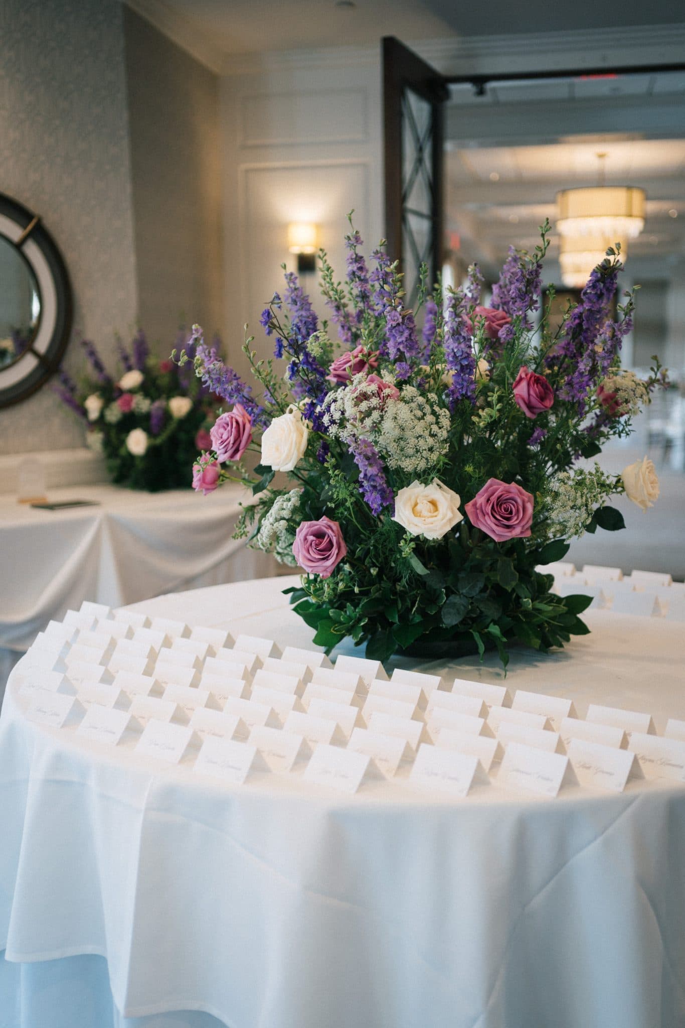 A round table is adorned with a floral centerpiece and neatly arranged white cards.