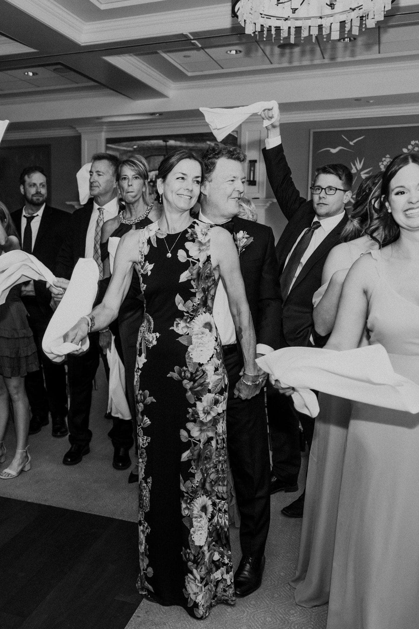 A group of people in formal attire holds white napkins, smiling and celebrating in a well-lit room.