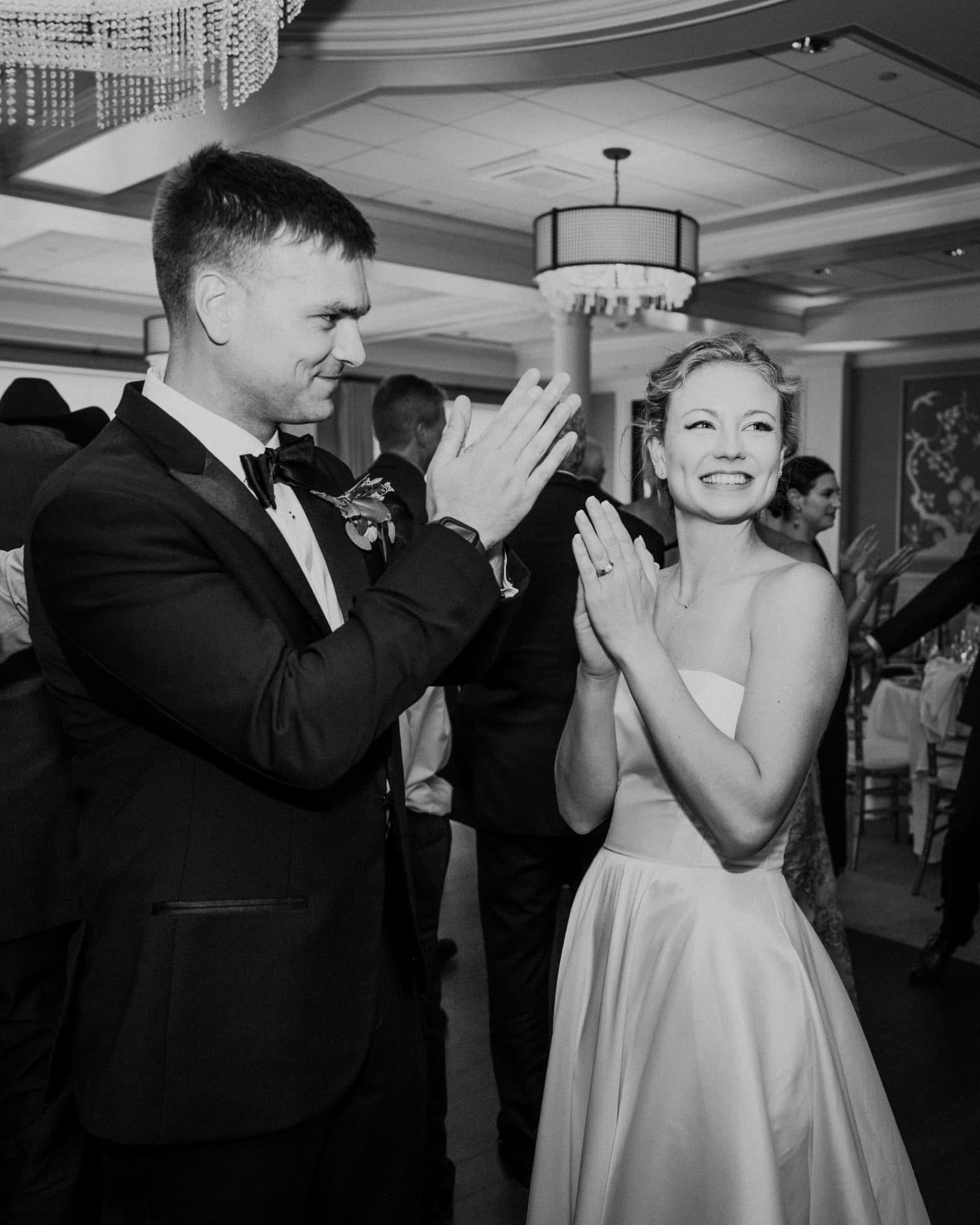 A man in a suit and a woman in a strapless dress clap together at a formal event.