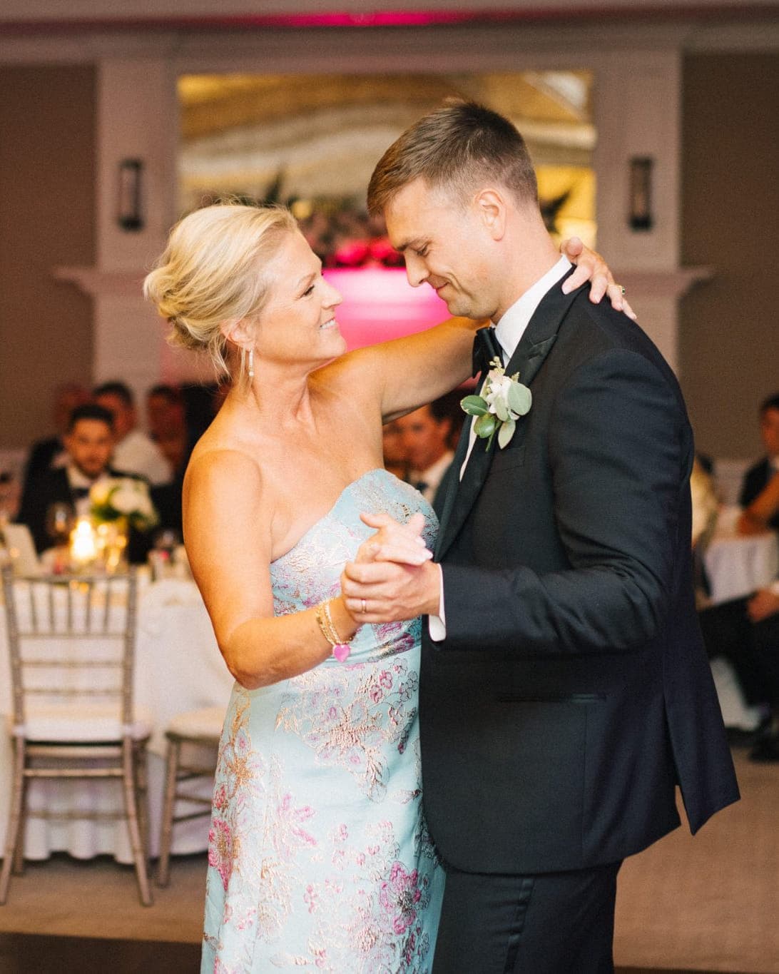A couple dances closely at a wedding reception, surrounded by guests seated at tables.