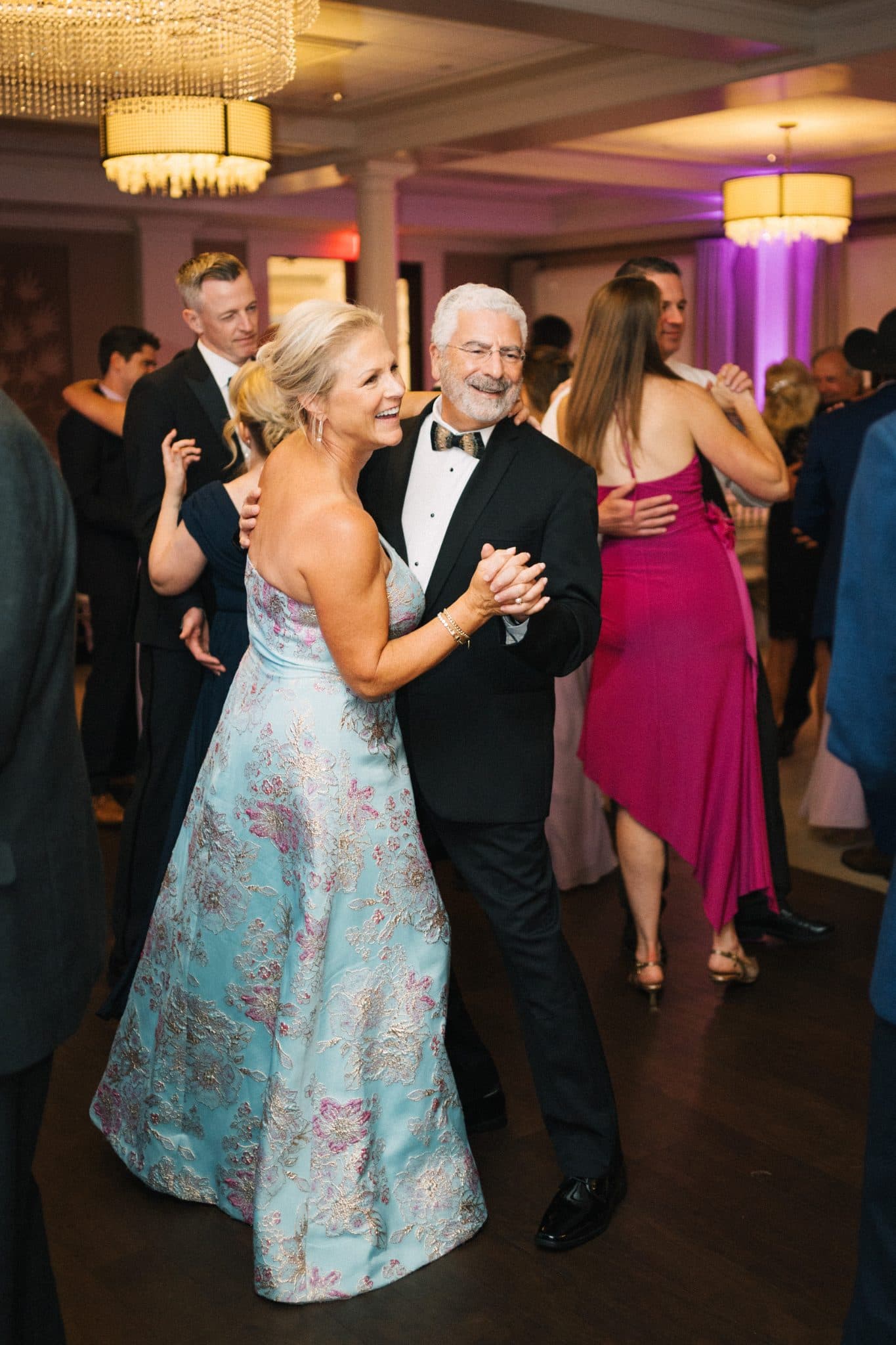 A couple dances together in a formal setting with other guests in the background.