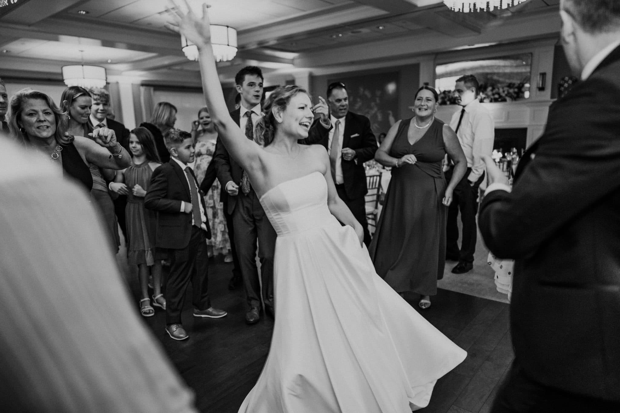 A bride in a strapless wedding dress dances joyfully on a crowded dance floor.
