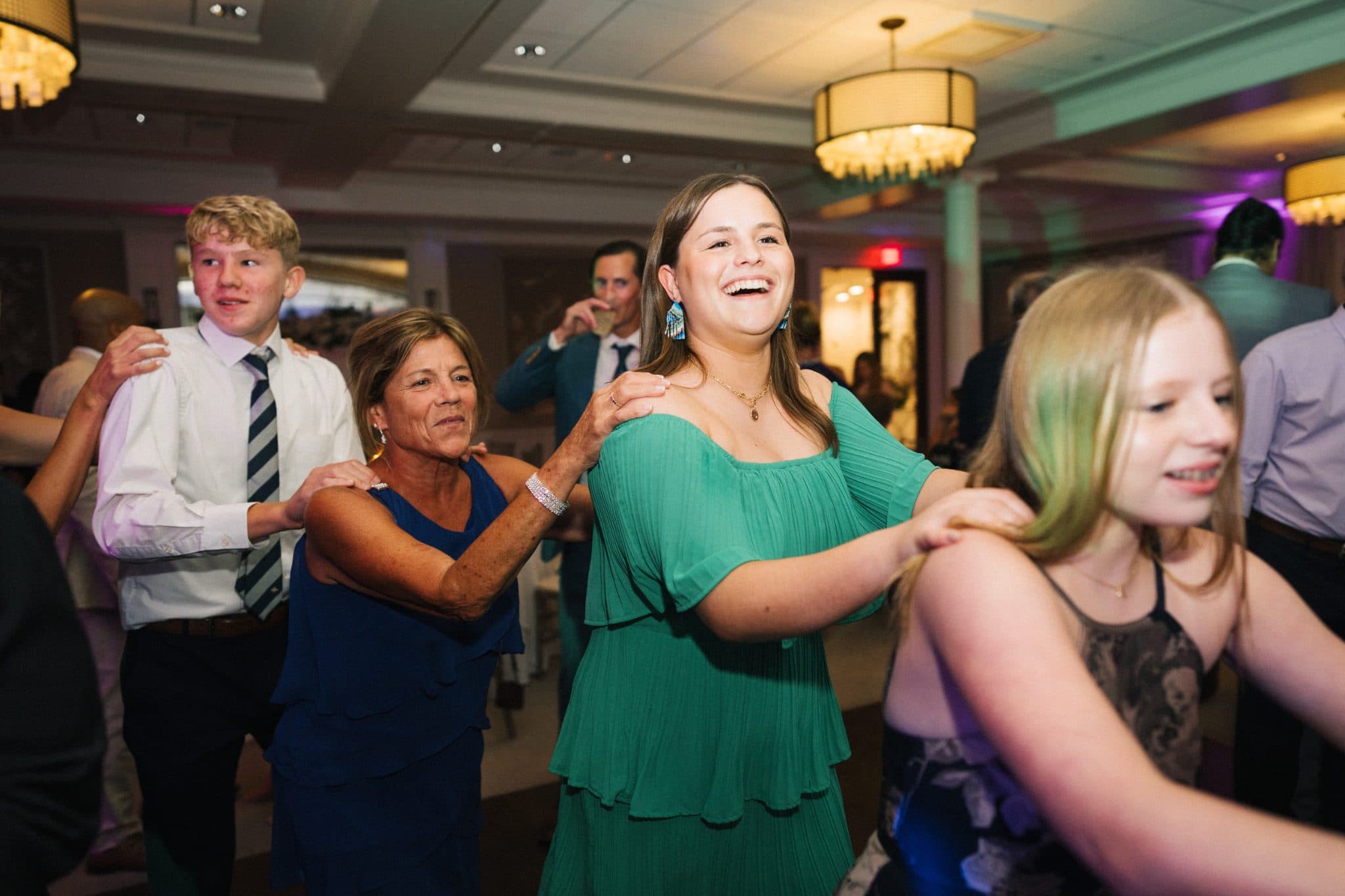 A group of people is dancing in a well-lit room with chandeliers.