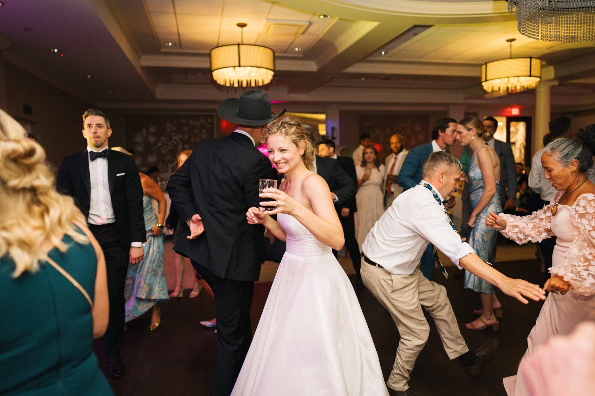 A bride in a white dress dances with a man in a white shirt and khaki pants at a lively wedding reception.