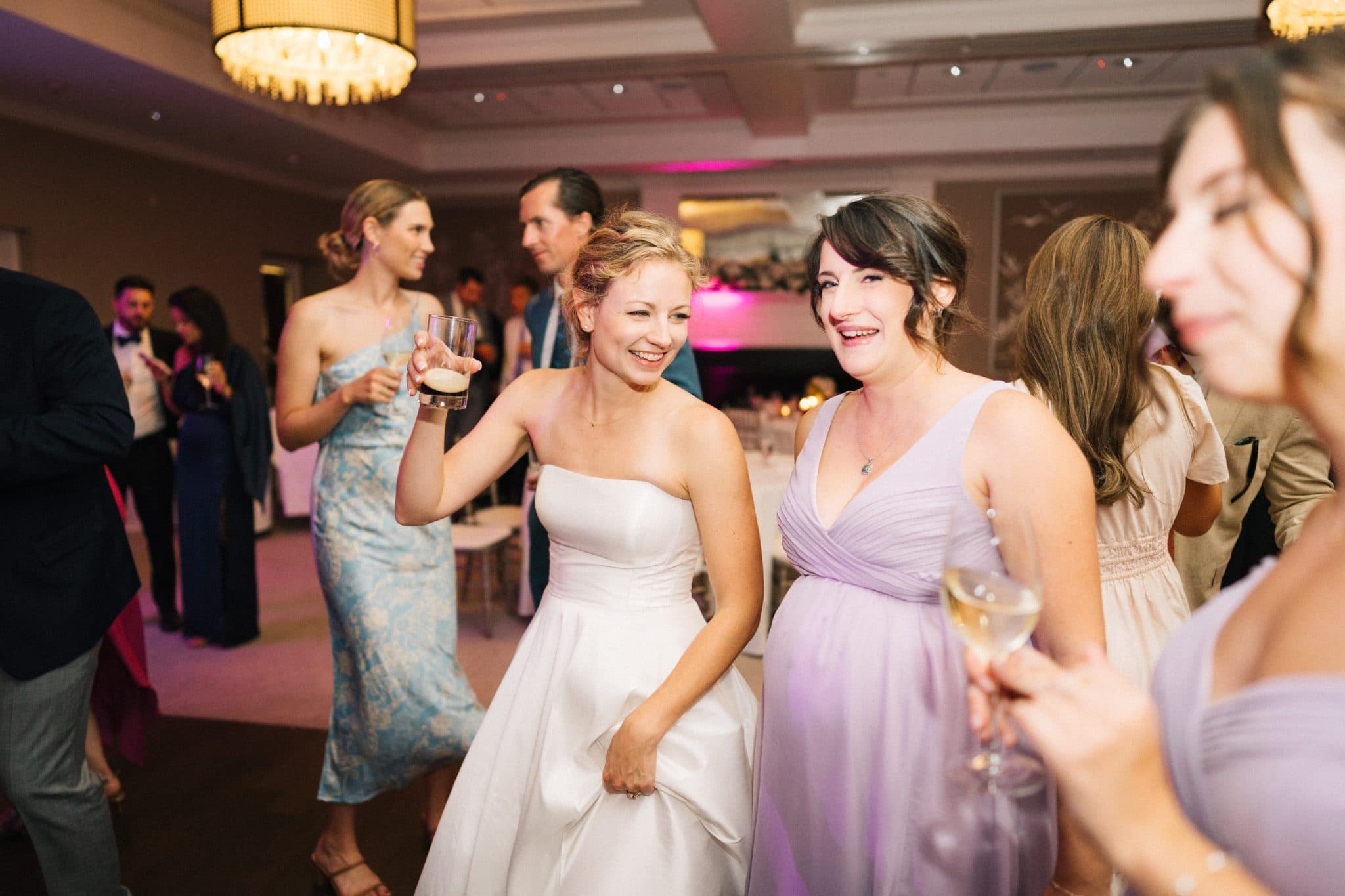 A bride in a white dress dances with a woman in a purple dress at a wedding reception.