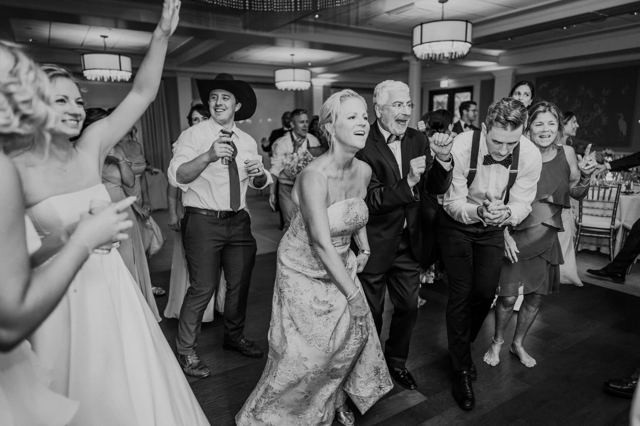 A bride in a strapless dress dances joyfully with guests in a lively wedding reception.