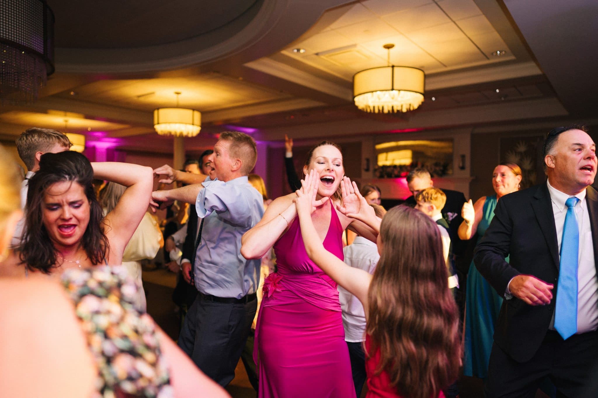 A lively wedding reception scene with people dancing and raising their hands in a festive atmosphere.