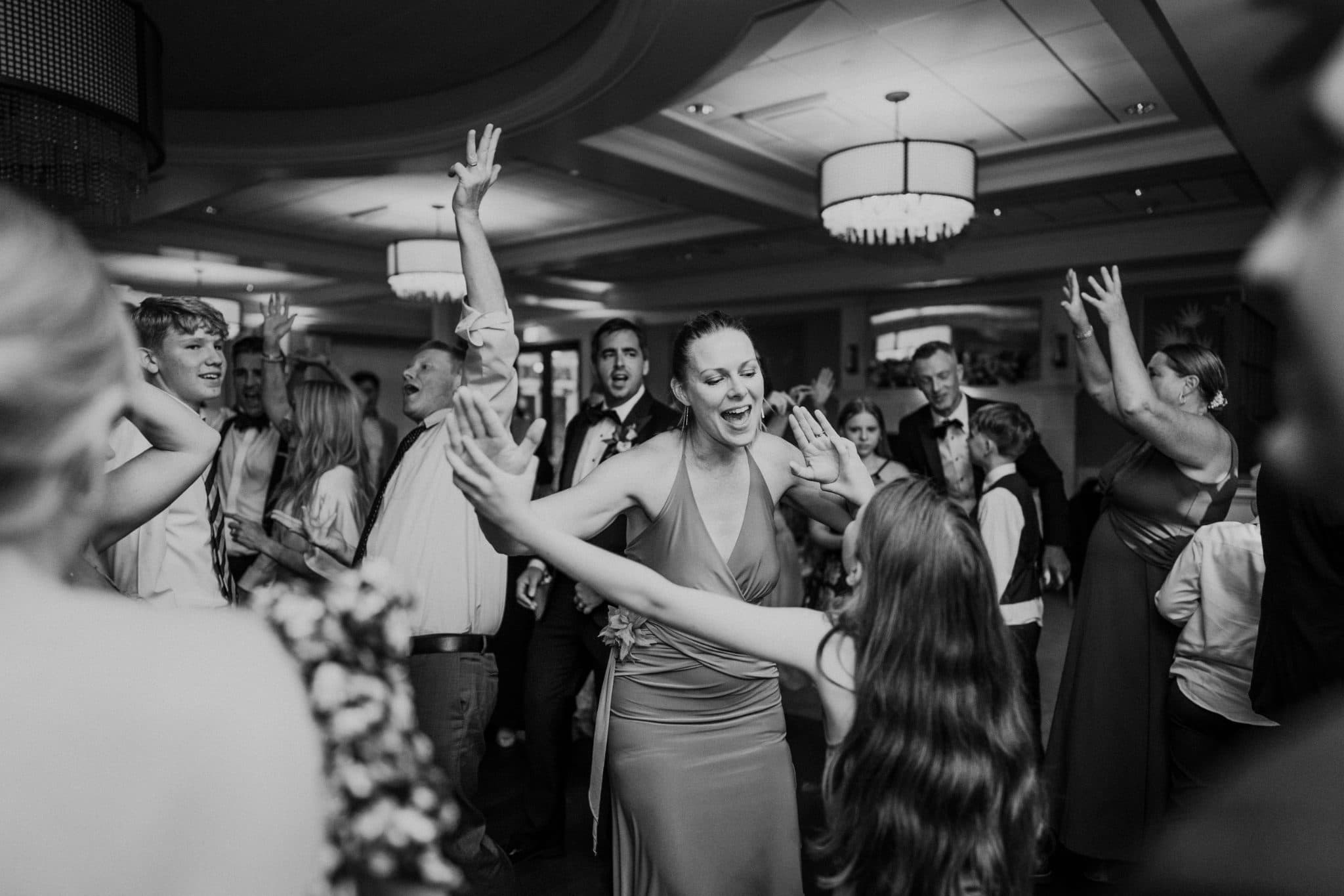 A lively wedding reception scene with guests dancing and raising their arms in celebration.