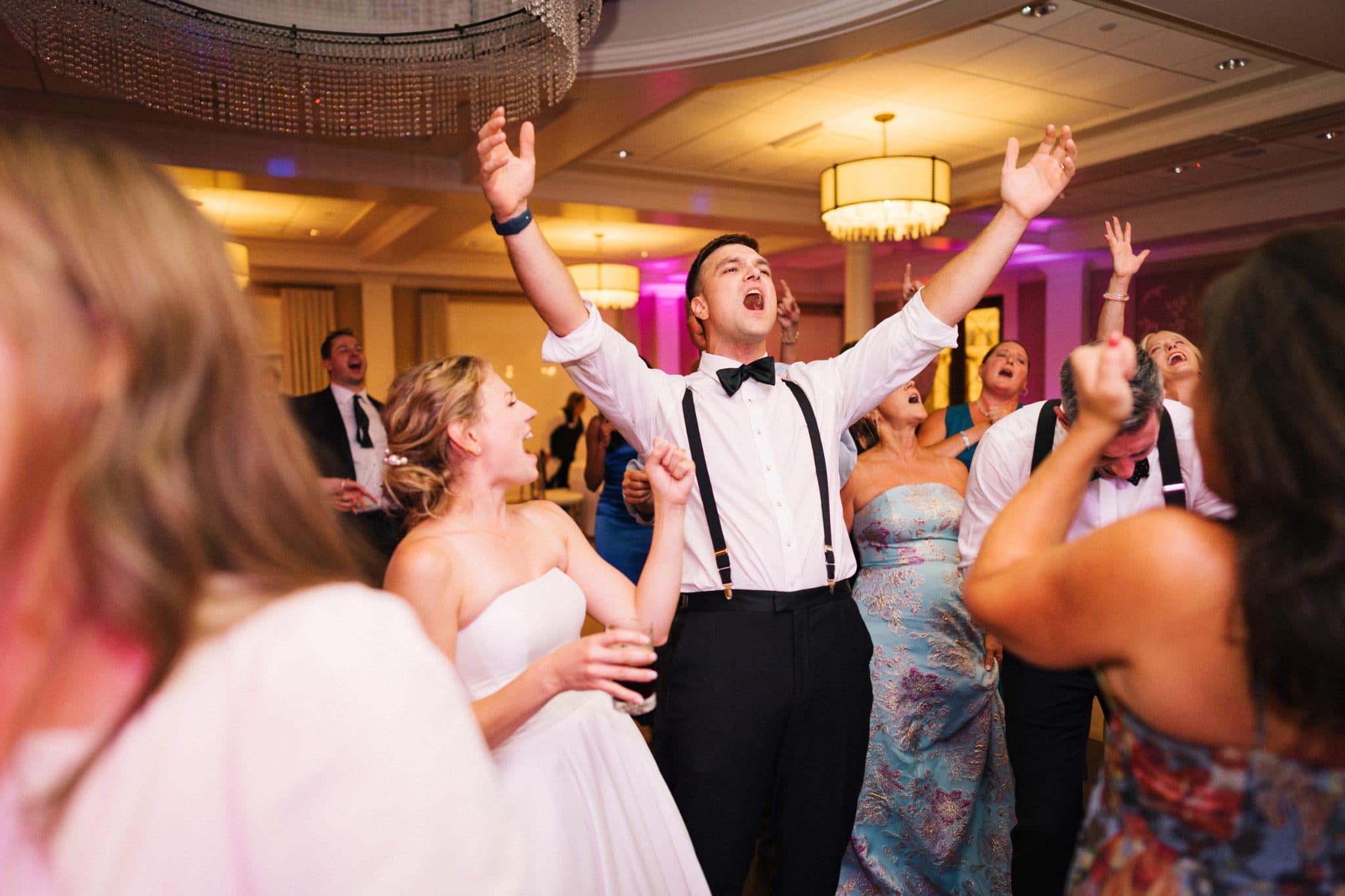A bride and groom dance joyfully on a crowded dance floor at a wedding reception.