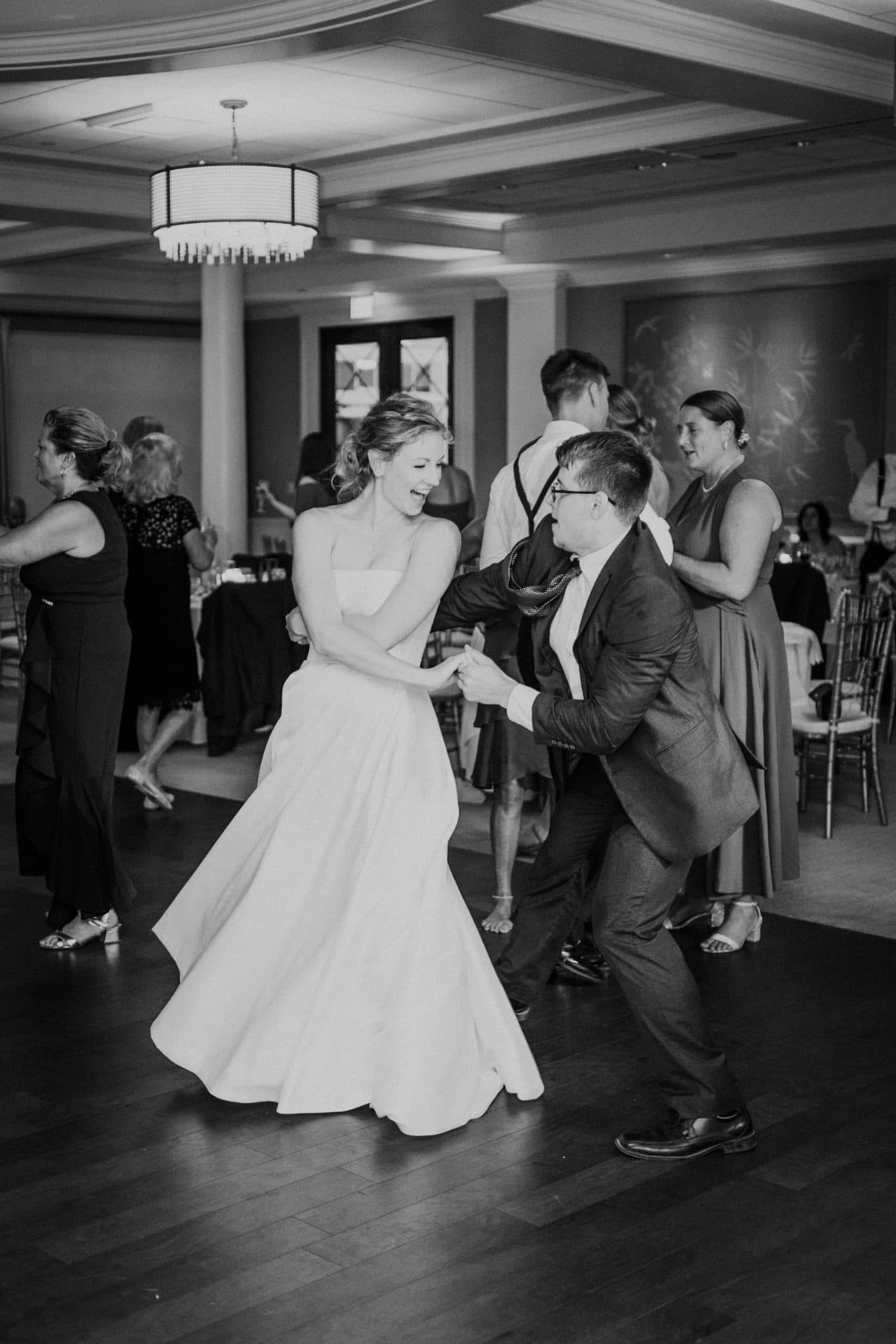 A bride in a strapless gown dances joyfully with a man in a suit at a wedding reception.