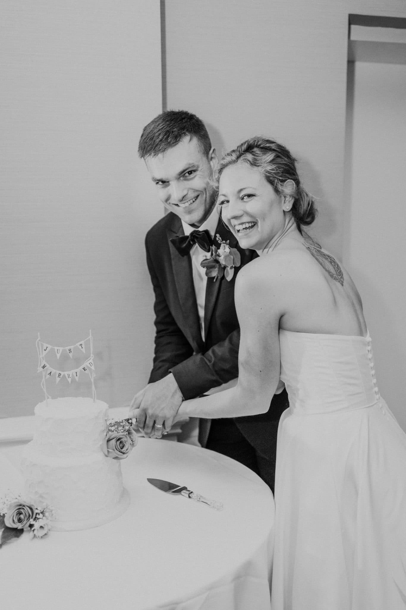 A bride and groom smile as they cut a wedding cake with a "Just Married" banner.