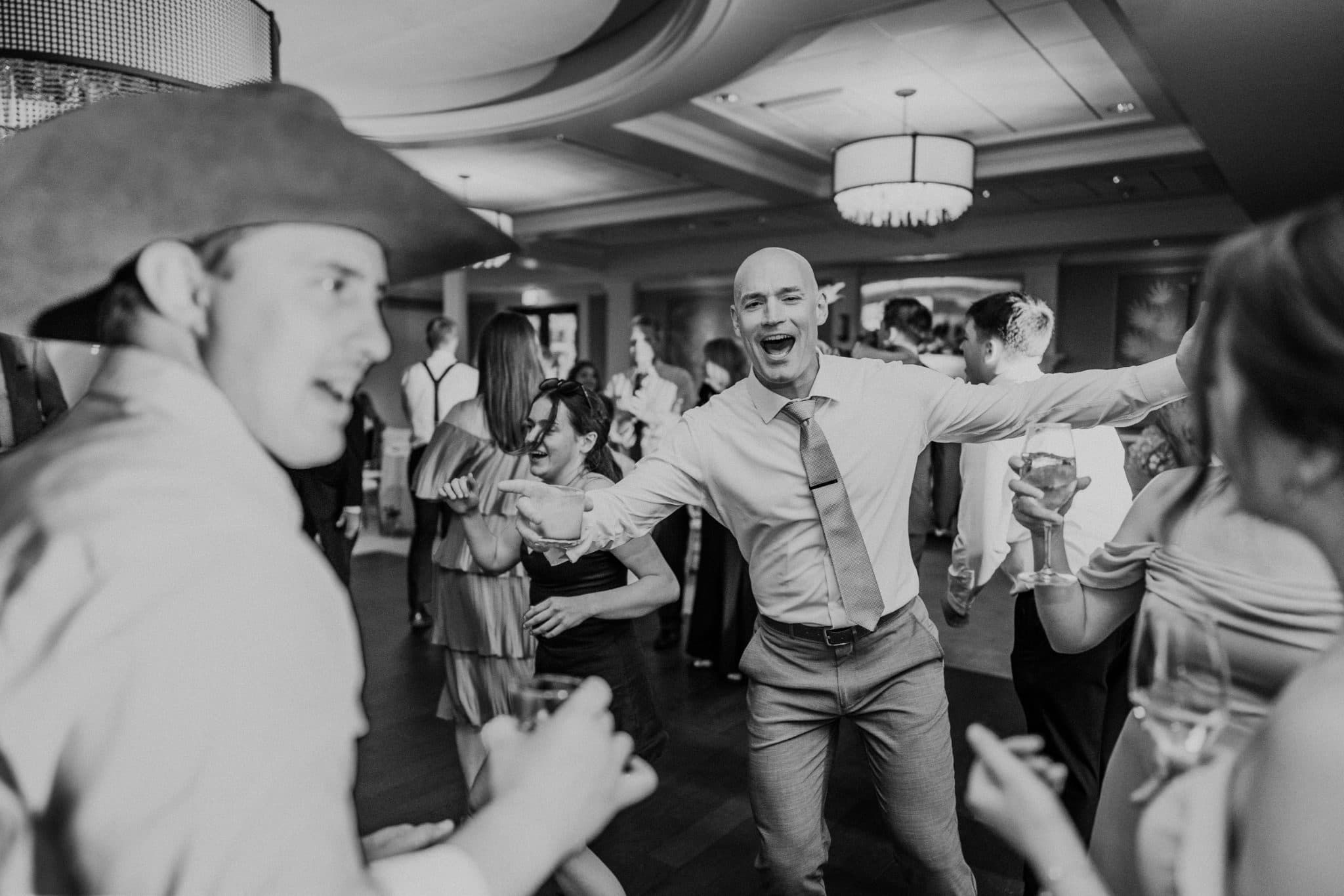 A man in a hat dances joyfully among guests at a lively wedding reception.