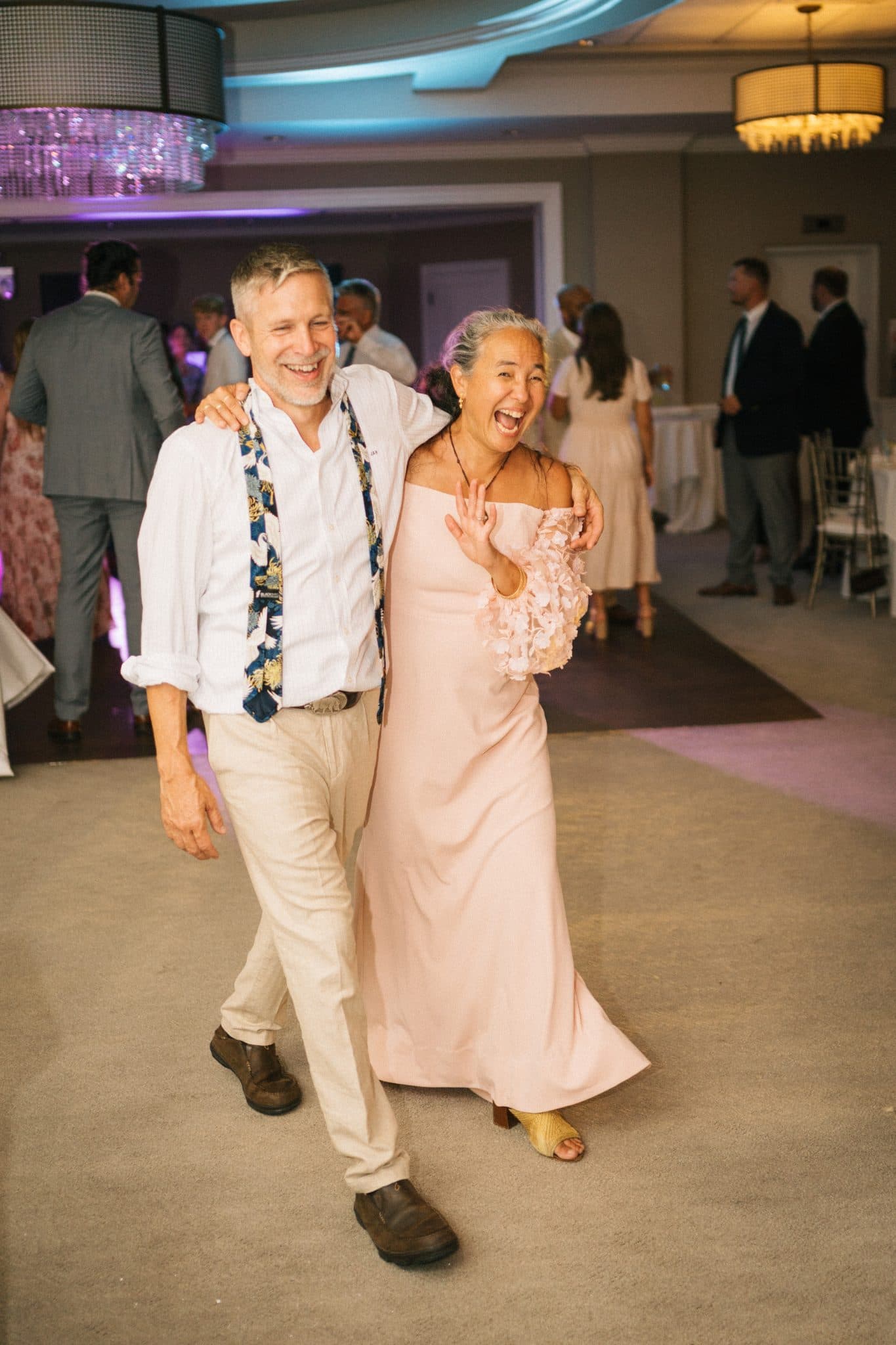 A man and woman dance joyfully on a dance floor, surrounded by other guests in a warmly lit room.