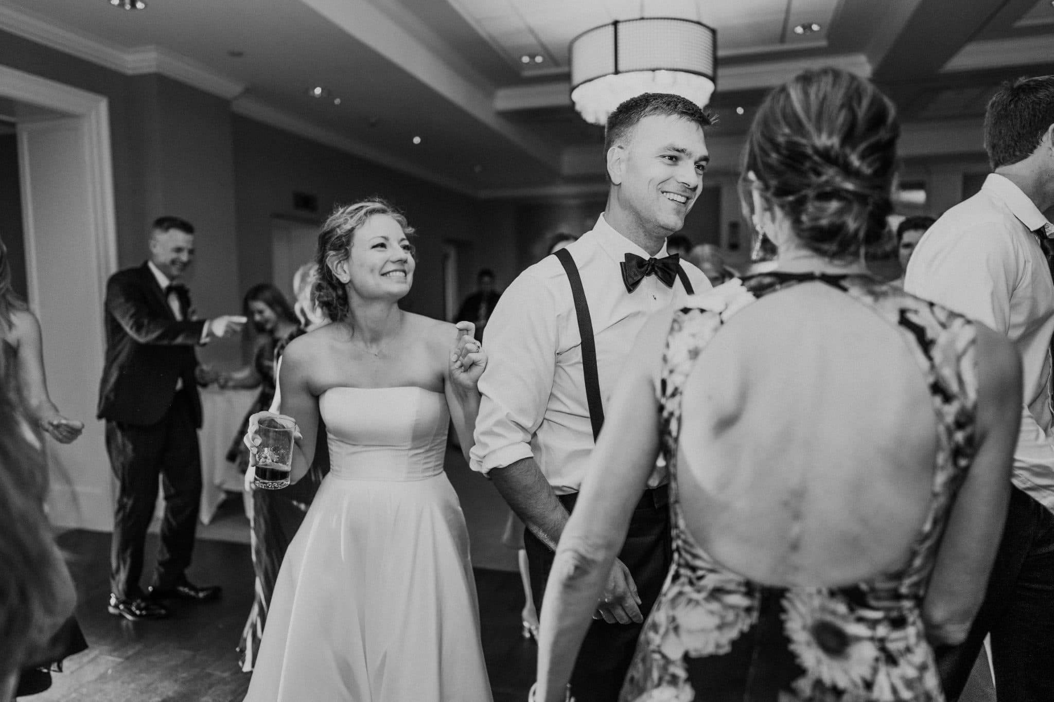 A bride in a strapless dress and a man in a white shirt and bow tie dance together at a wedding reception.