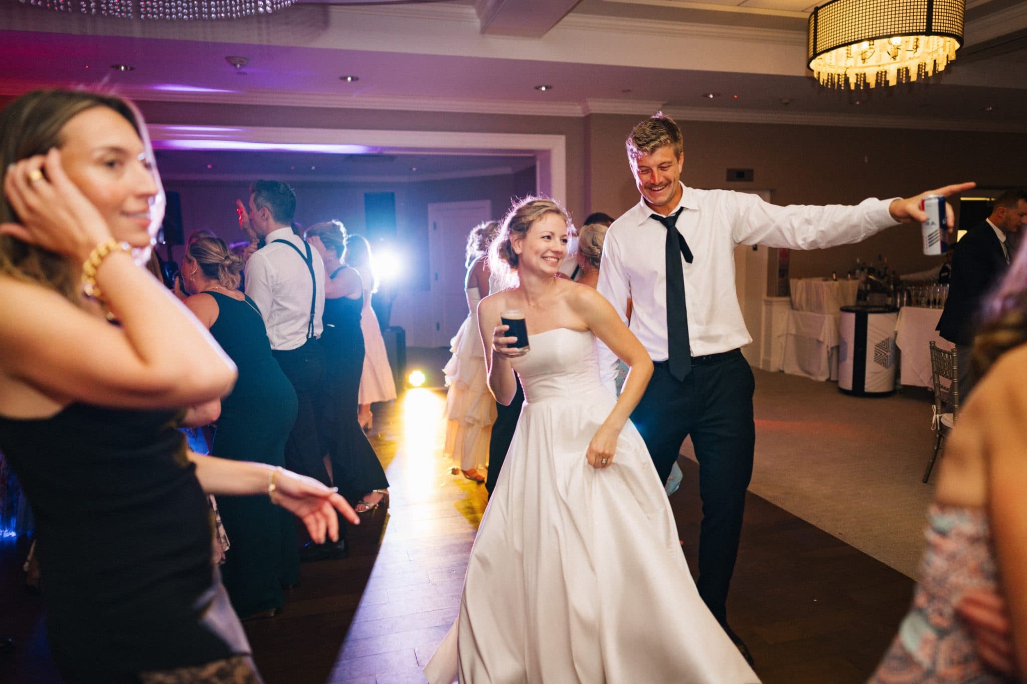 A bride and groom dance joyfully on a wedding reception floor, surrounded by guests.