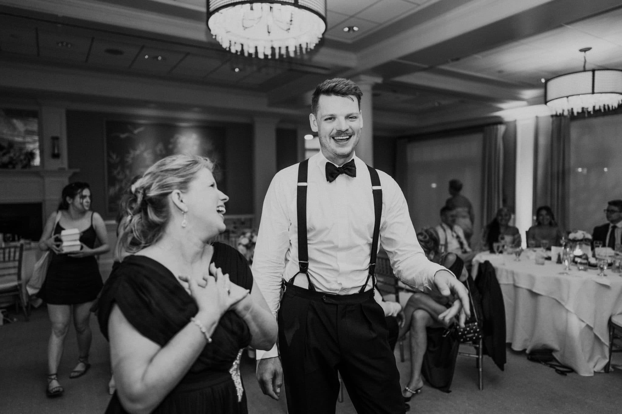 A man in a bow tie and suspenders dances with a woman in a black dress in a formal setting.