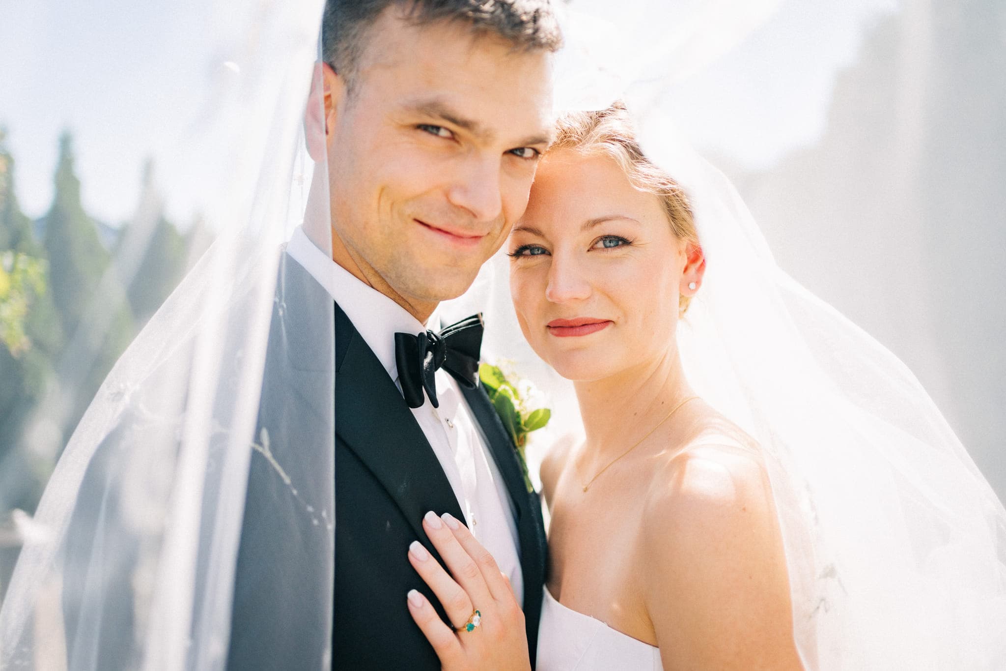 A bride and groom stand close, the bride's hand on the groom's chest, both under a veil.