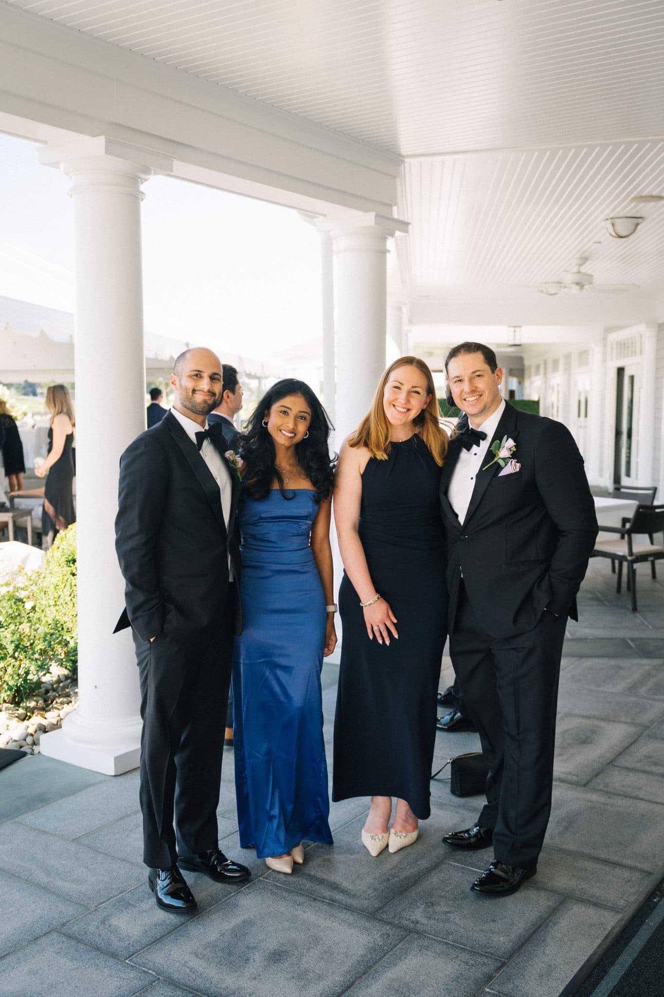 Four individuals in formal attire stand together on a tiled porch, smiling for a photograph.