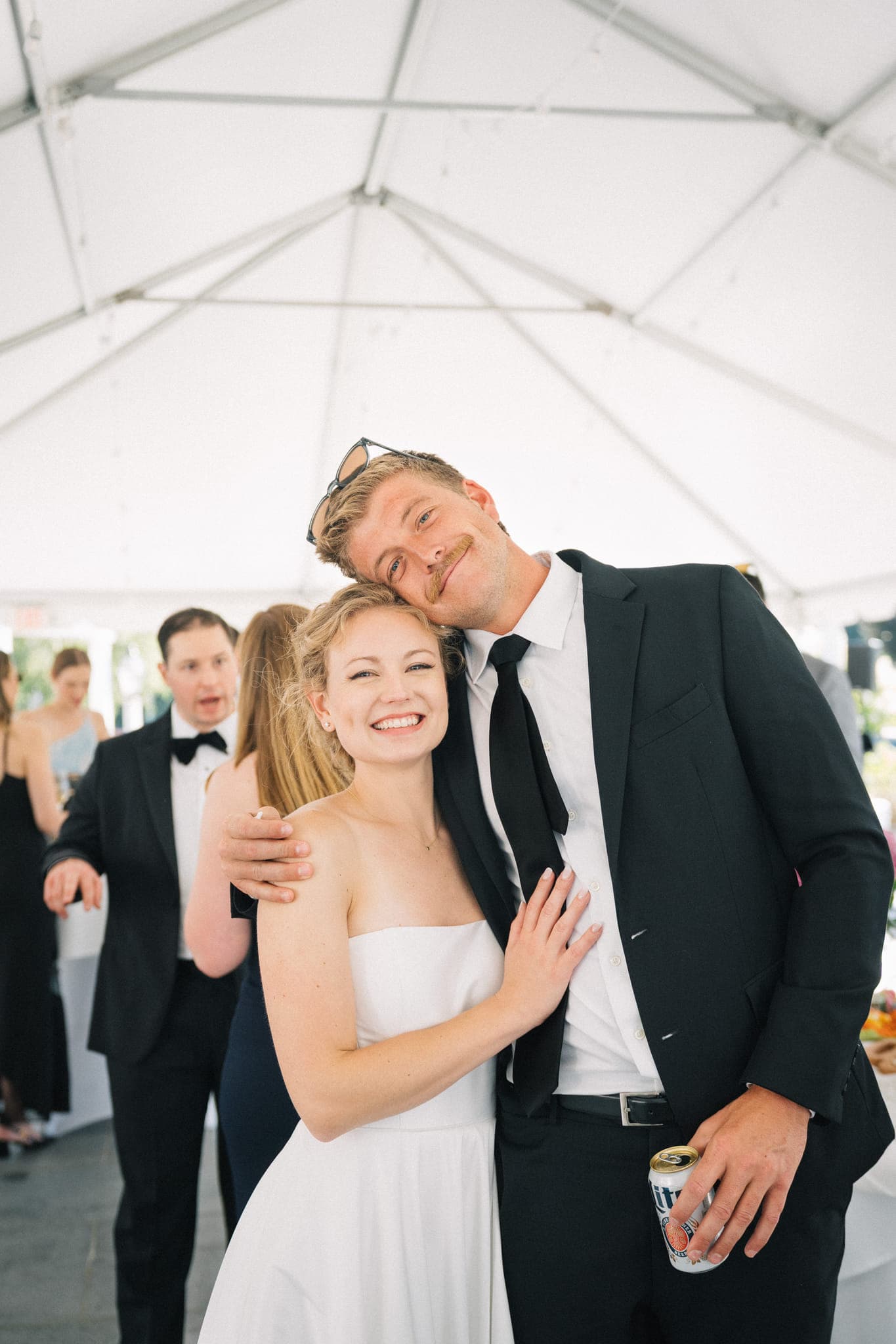 A bride in a white dress hugs a man in a black suit under a white tent.