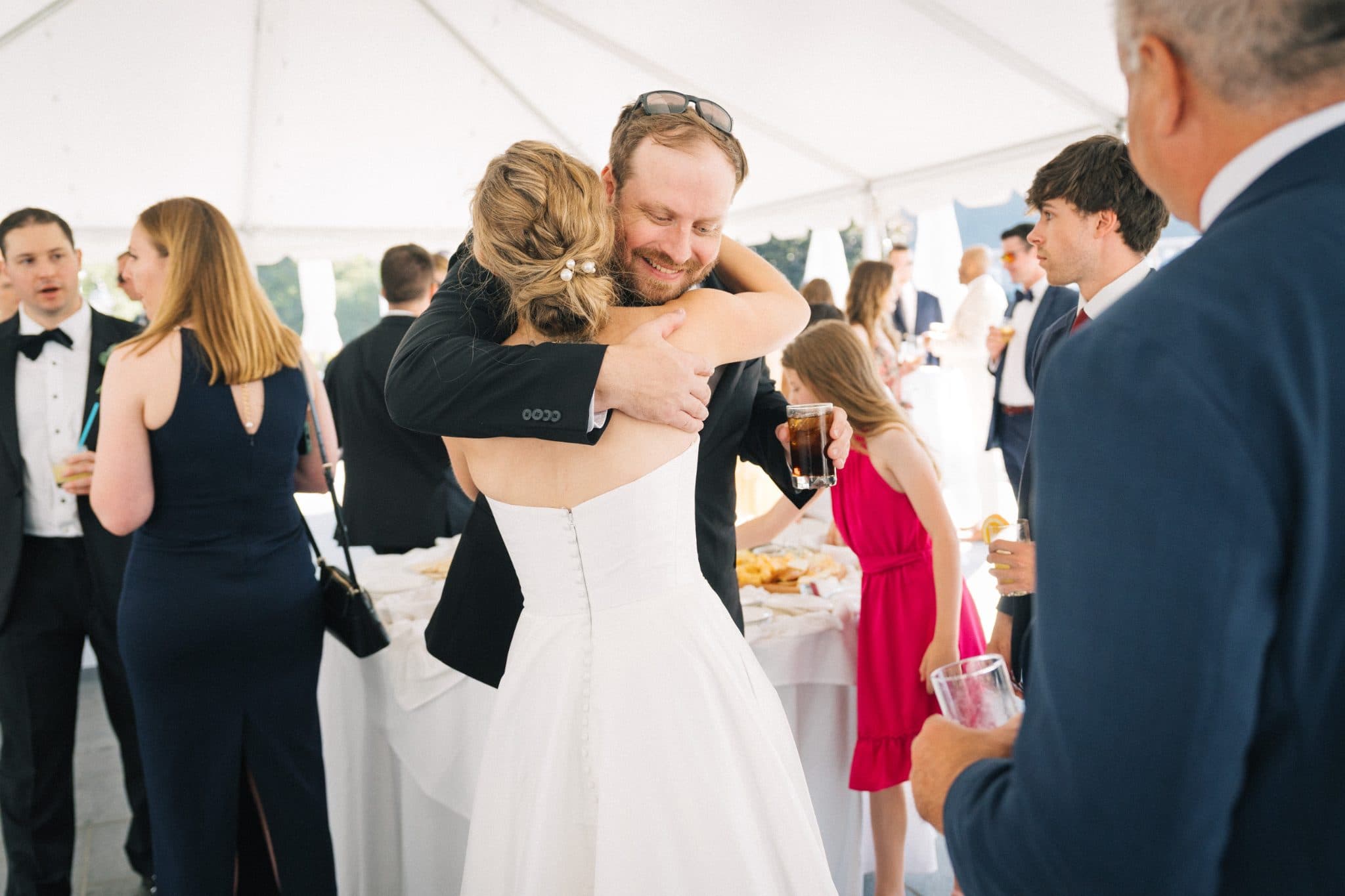 A bride and groom share a heartfelt embrace at a wedding reception under a white tent.
