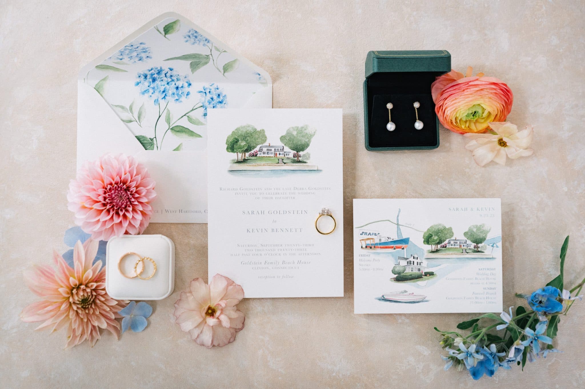 A wedding invitation set with floral envelopes, flowers, a ring box, earrings, and a small box with a ring.