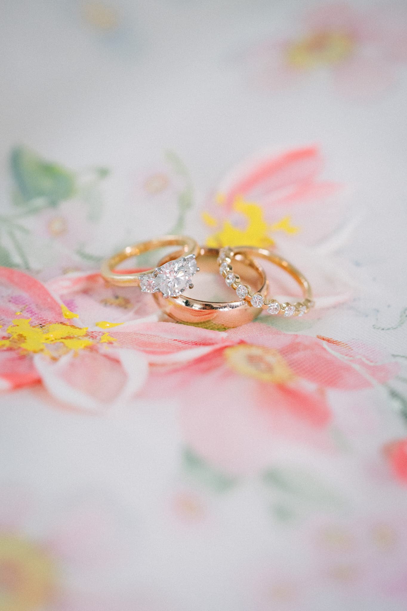 Three rings with diamonds rest on a floral-patterned fabric.