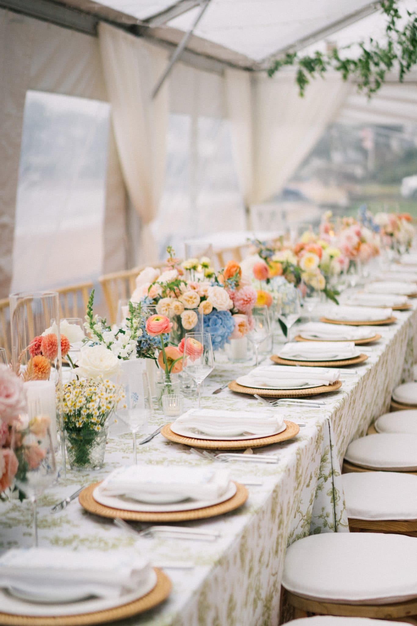 A long table is set for a wedding reception with floral centerpieces, white plates, and neatly arranged silverware.