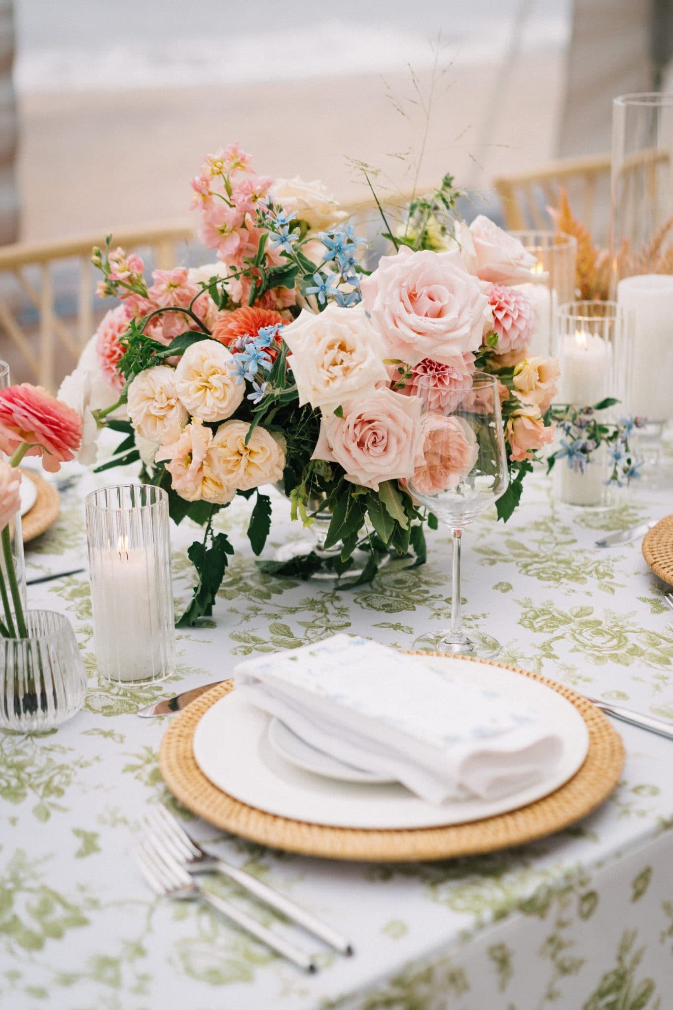 A beautifully set table with pastel flowers, greenery, candles, and elegant place settings.