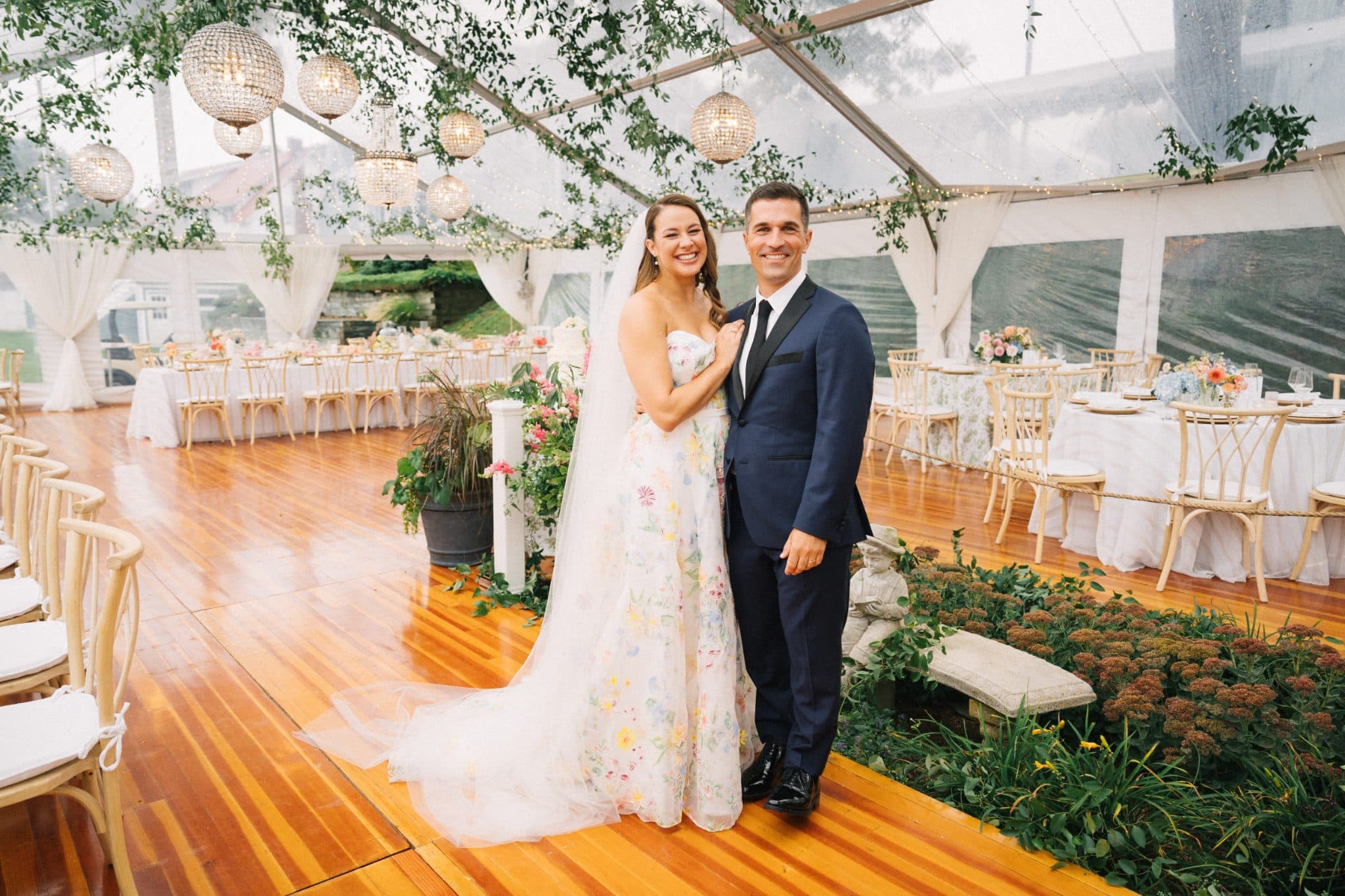 A couple stands together in a beautifully decorated wedding reception with floral arrangements and elegant decor.