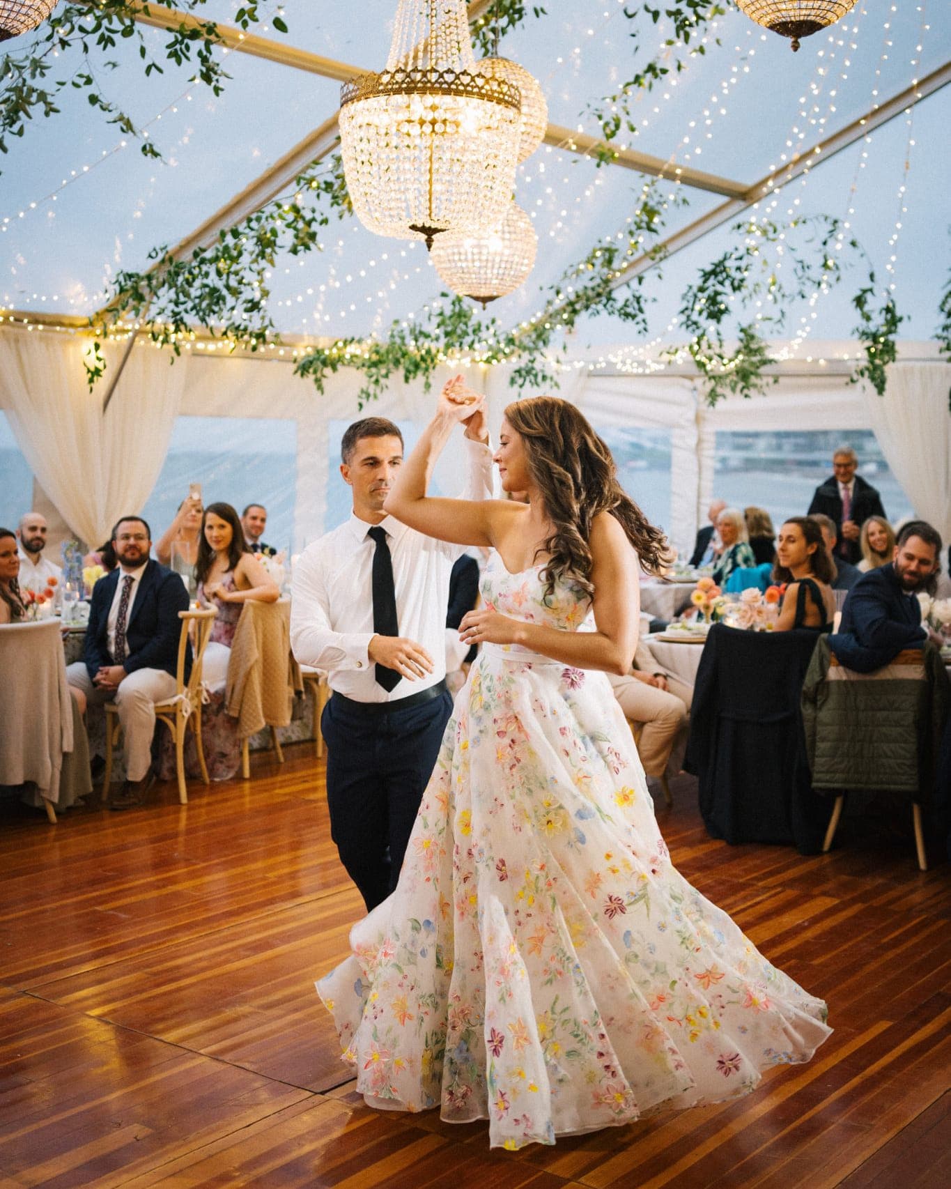 A couple dances under a canopy of lights and greenery at a wedding reception.