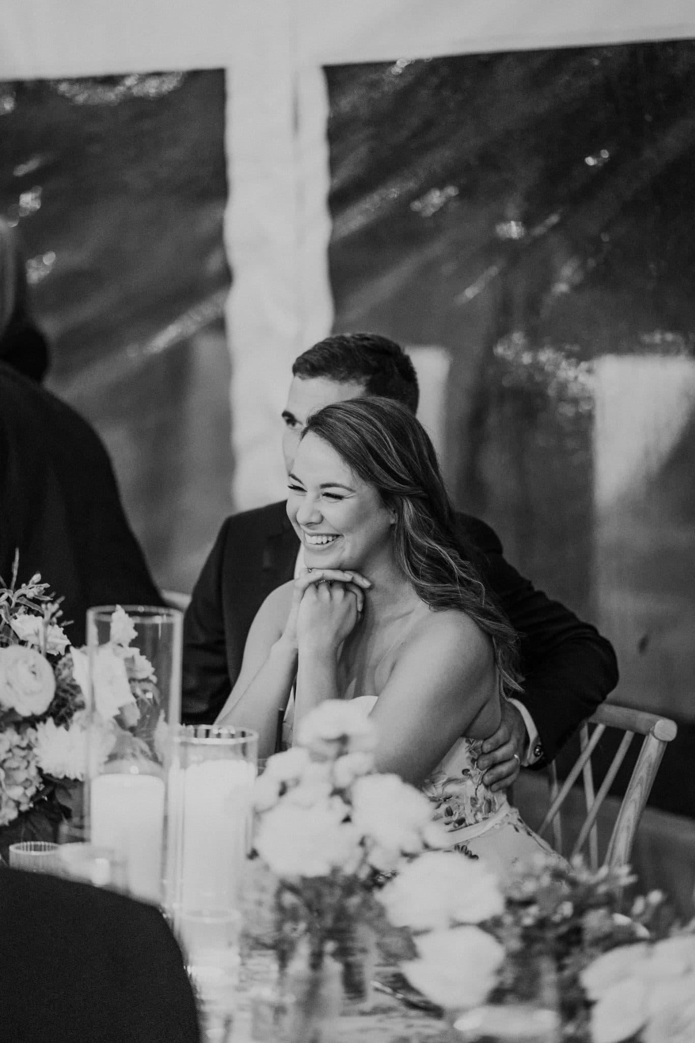 A bride smiles at a guest at a wedding reception, surrounded by floral arrangements and candles.