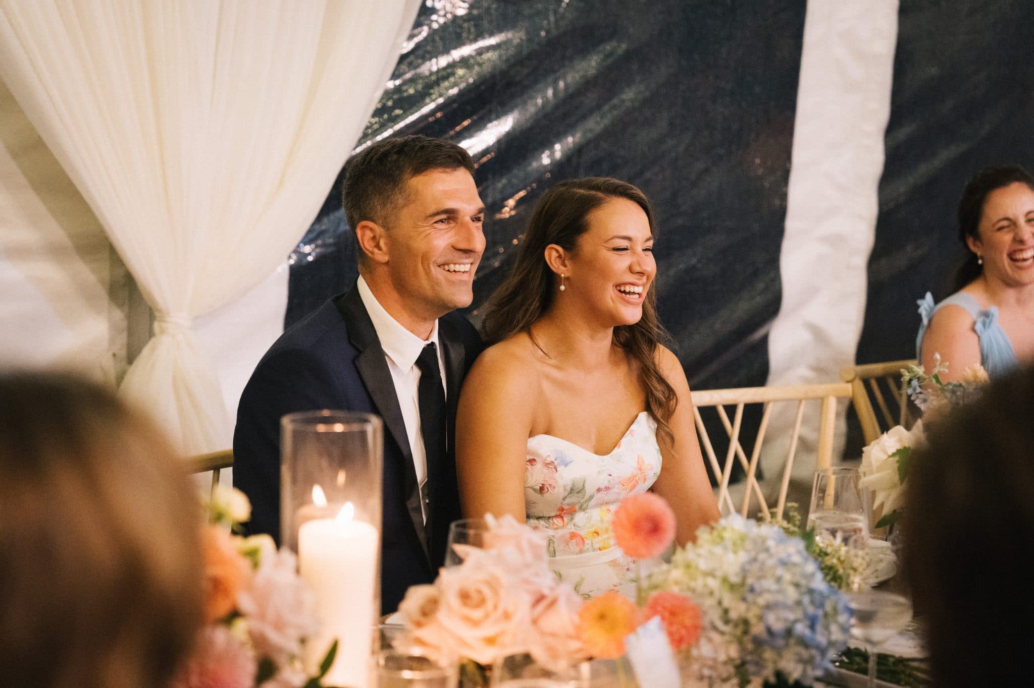 A bride and groom smile at a wedding reception table adorned with flowers and candles.