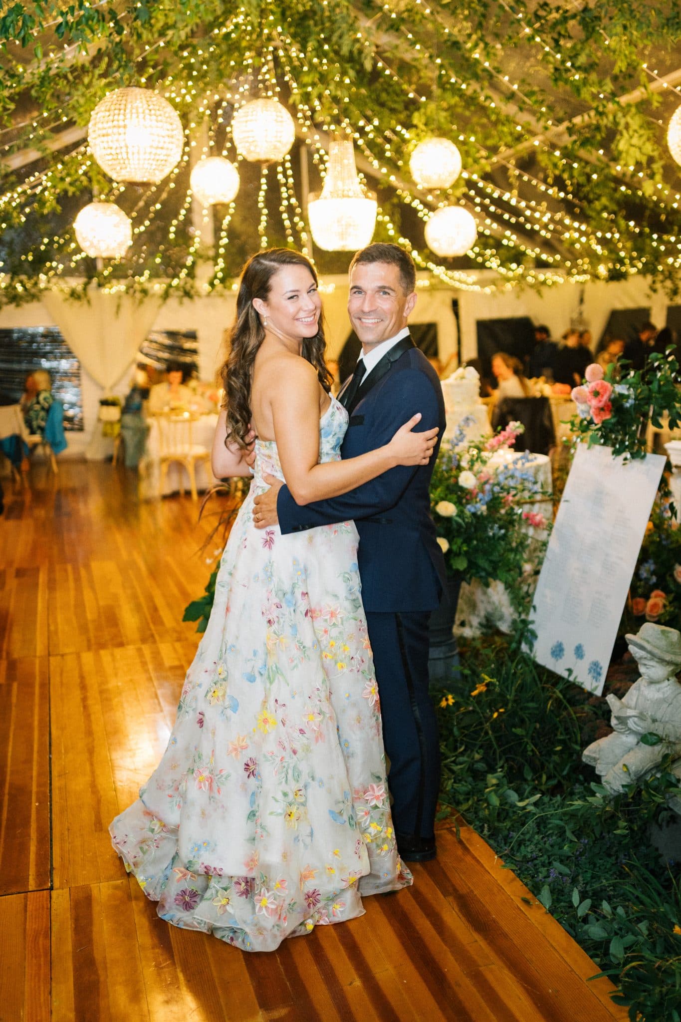 A couple embraces under a canopy of lights and greenery at a wedding reception.