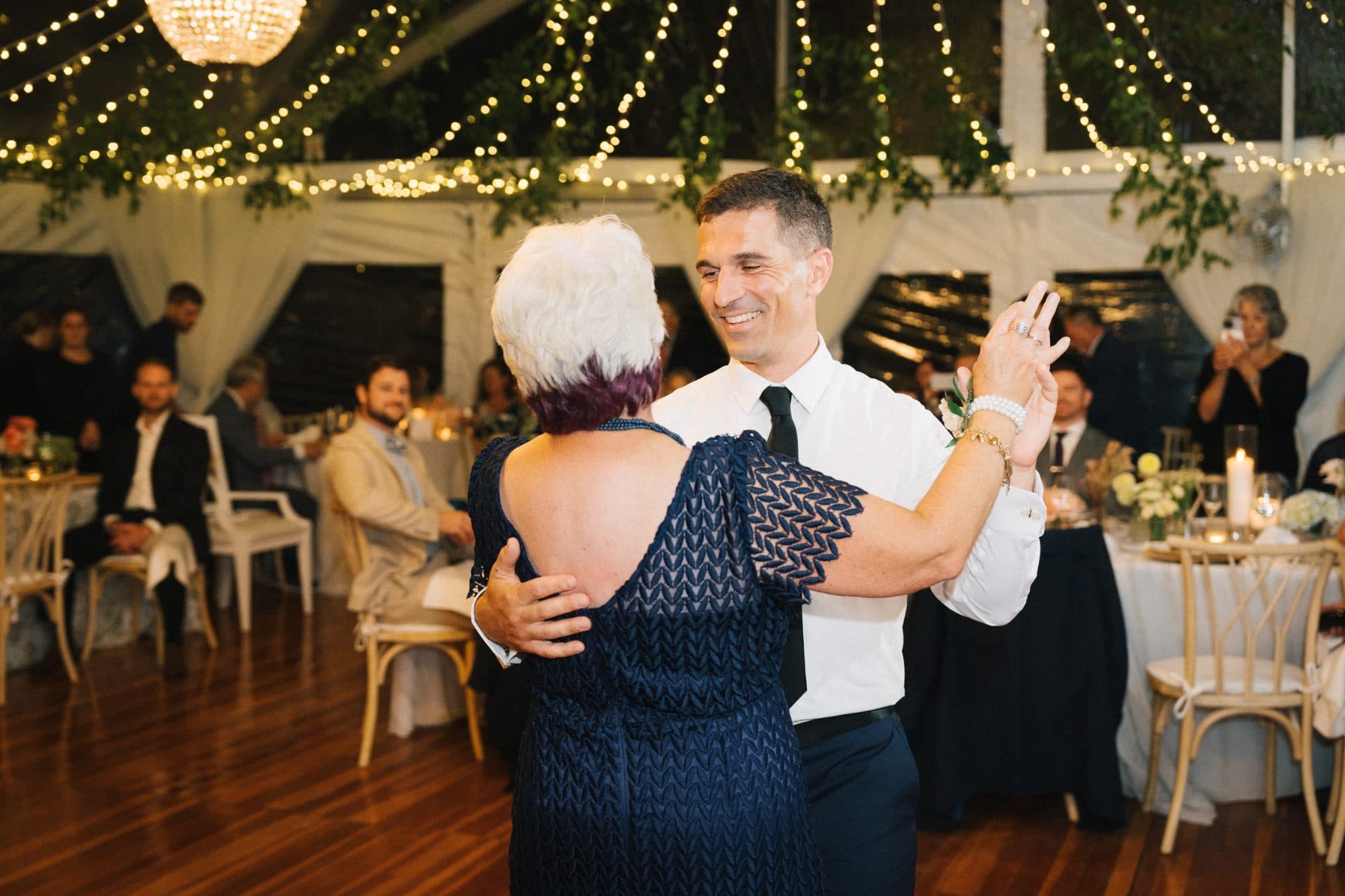 A man and woman dance together at a wedding reception under string lights.