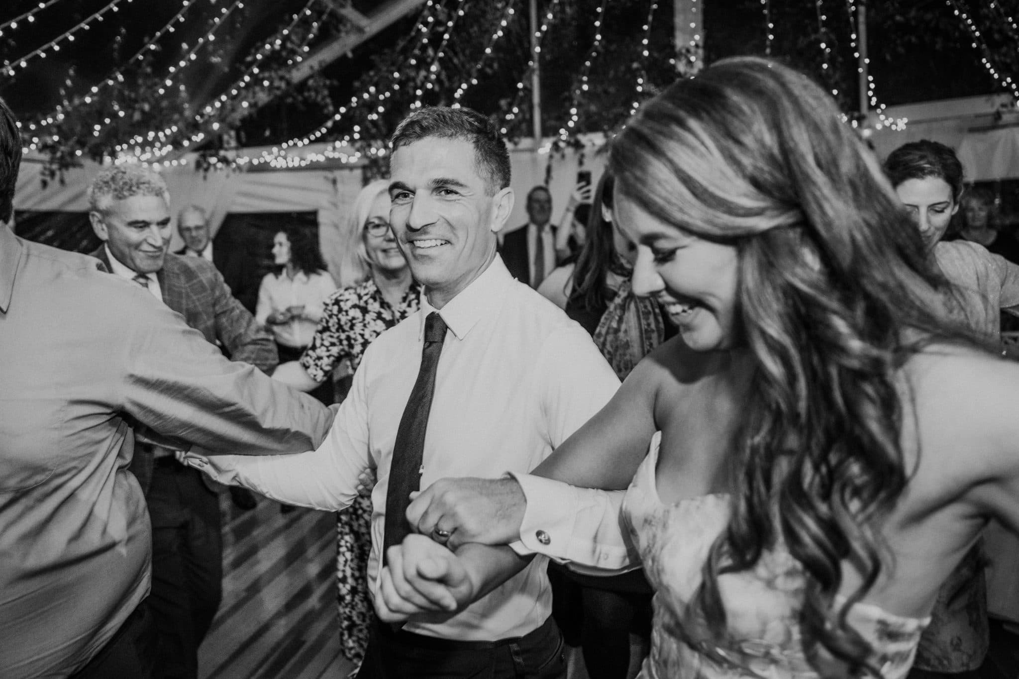 A man and a woman dance together at a lively wedding reception under string lights.