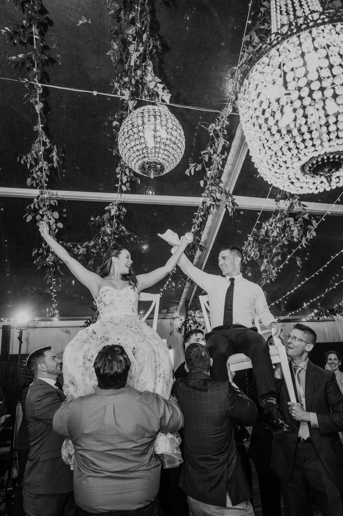 A bride and groom are lifted on guests' shoulders in a festive wedding celebration.