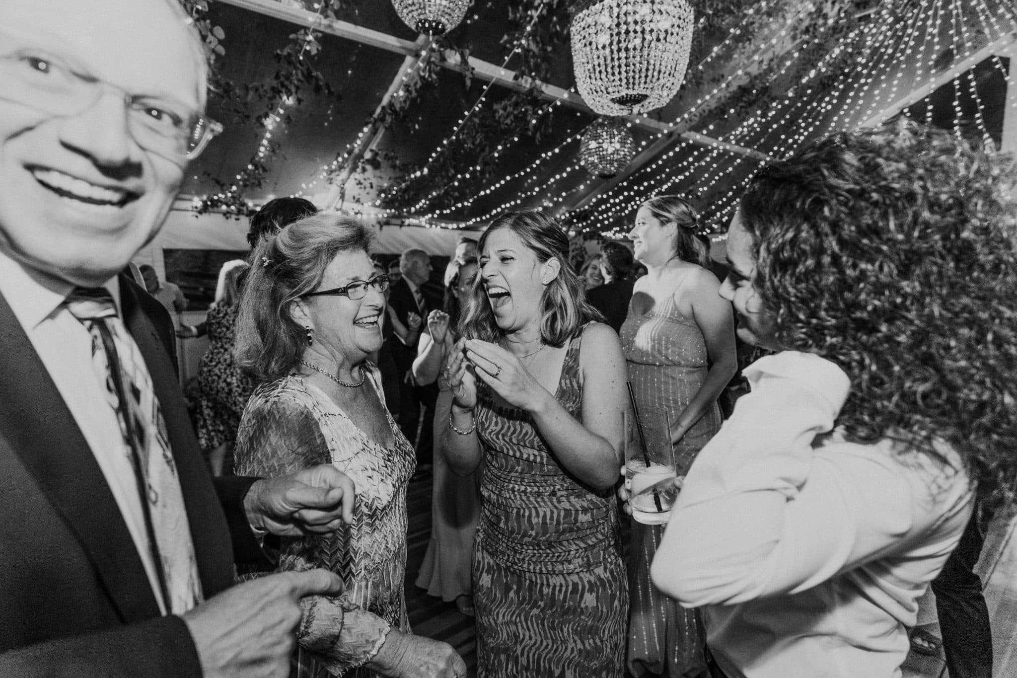 A group of people in a tent decorated with lights and chandeliers, smiling and laughing together.
