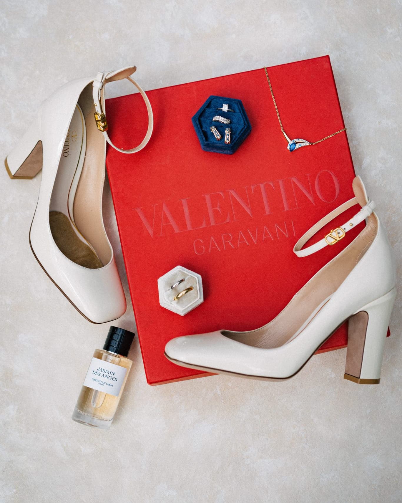 A red Valentino Garavani box with jewelry and a pair of cream heels is displayed on a light surface.