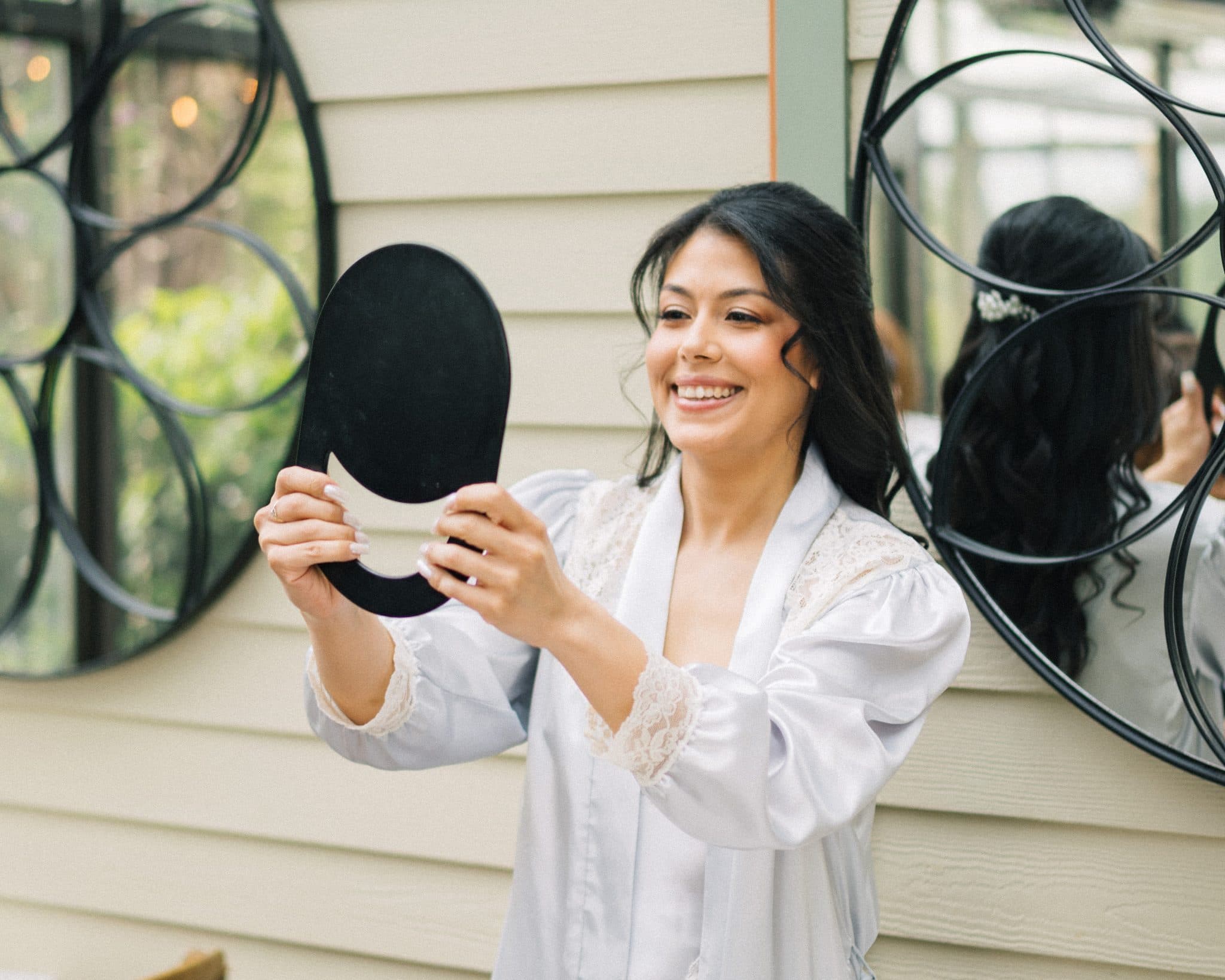 A woman in a white robe holds a small mirror, smiling as she looks at her reflection.