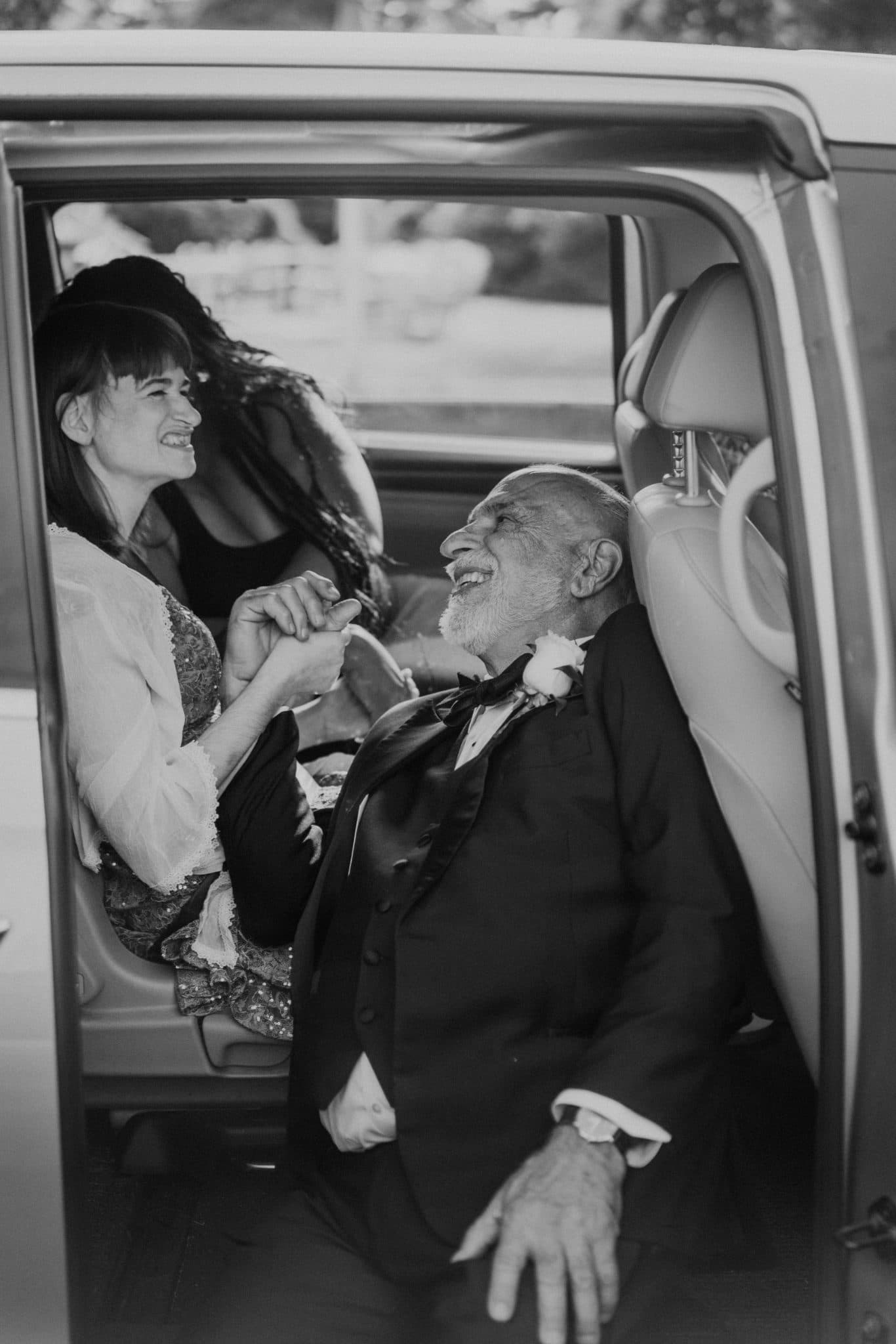 A bride and groom share a joyful moment inside a vintage car.