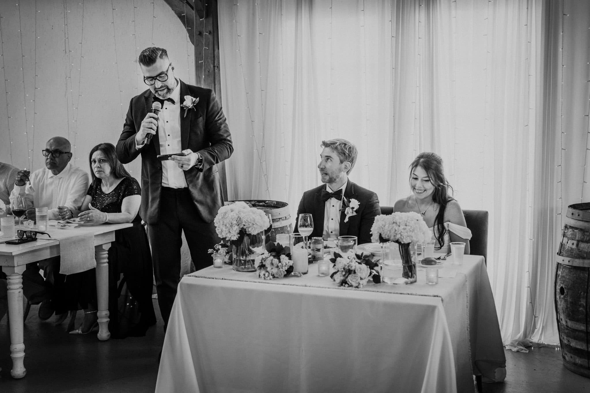A man in a suit stands at a podium addressing a seated couple at a decorated table.
