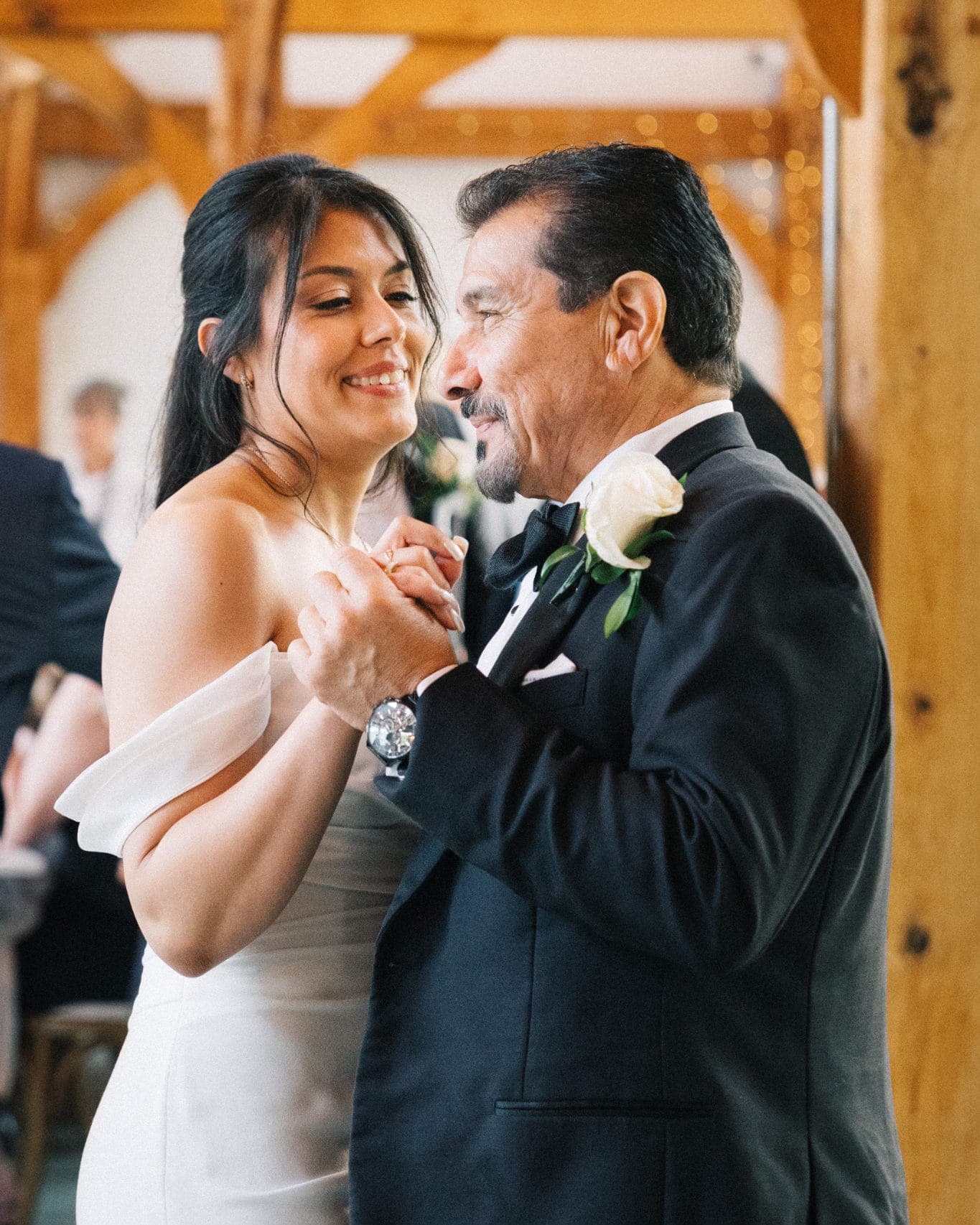 A bride in a white dress and a man in a black suit share a dance, holding hands and smiling.