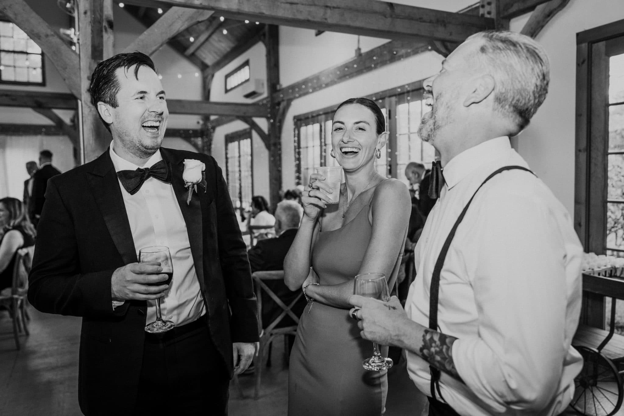 Three people in formal attire share a moment of laughter and conversation at a wedding reception.