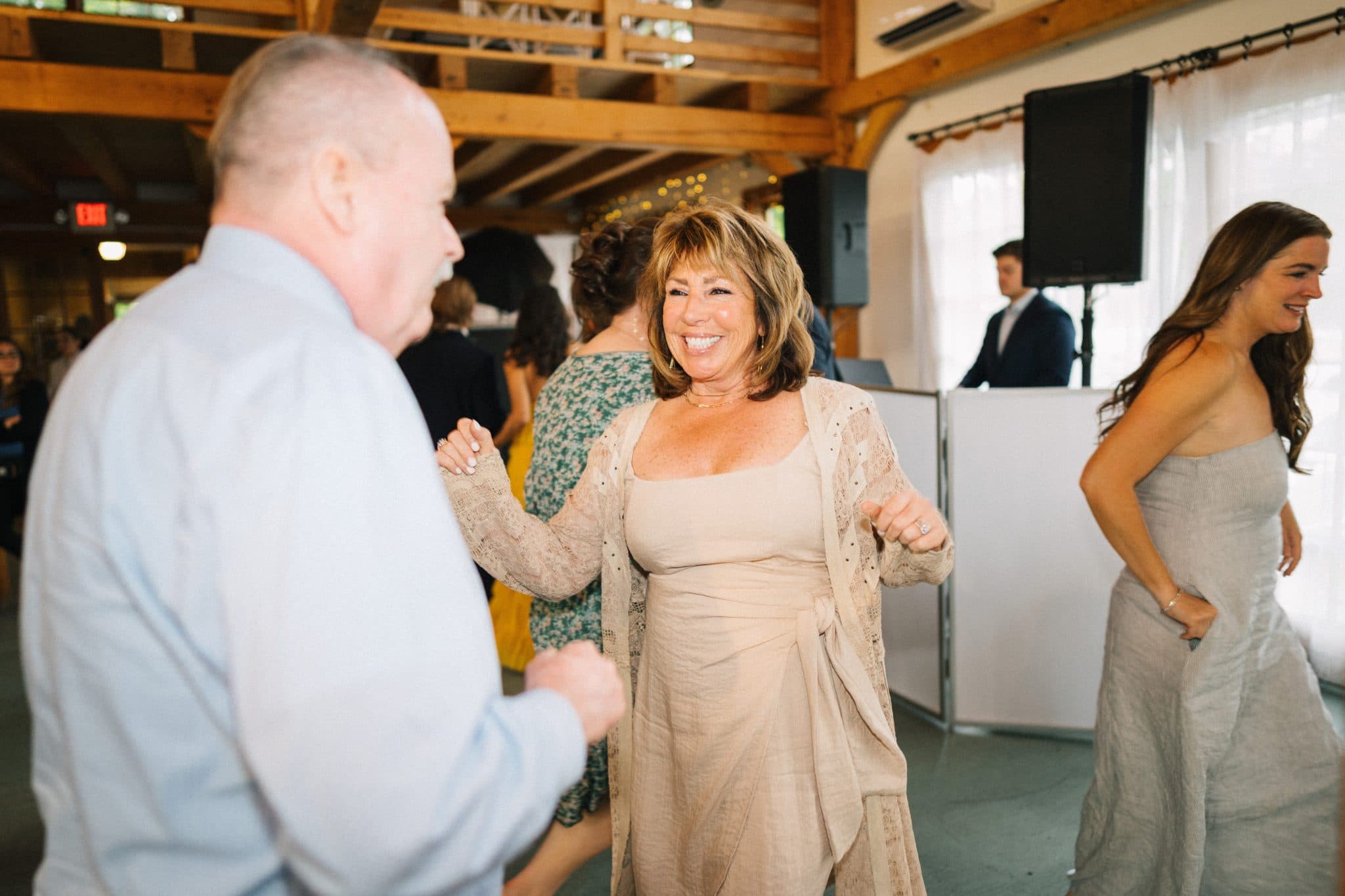 A woman in a beige dress dances joyfully with a man in a light blue shirt at a wedding reception.
