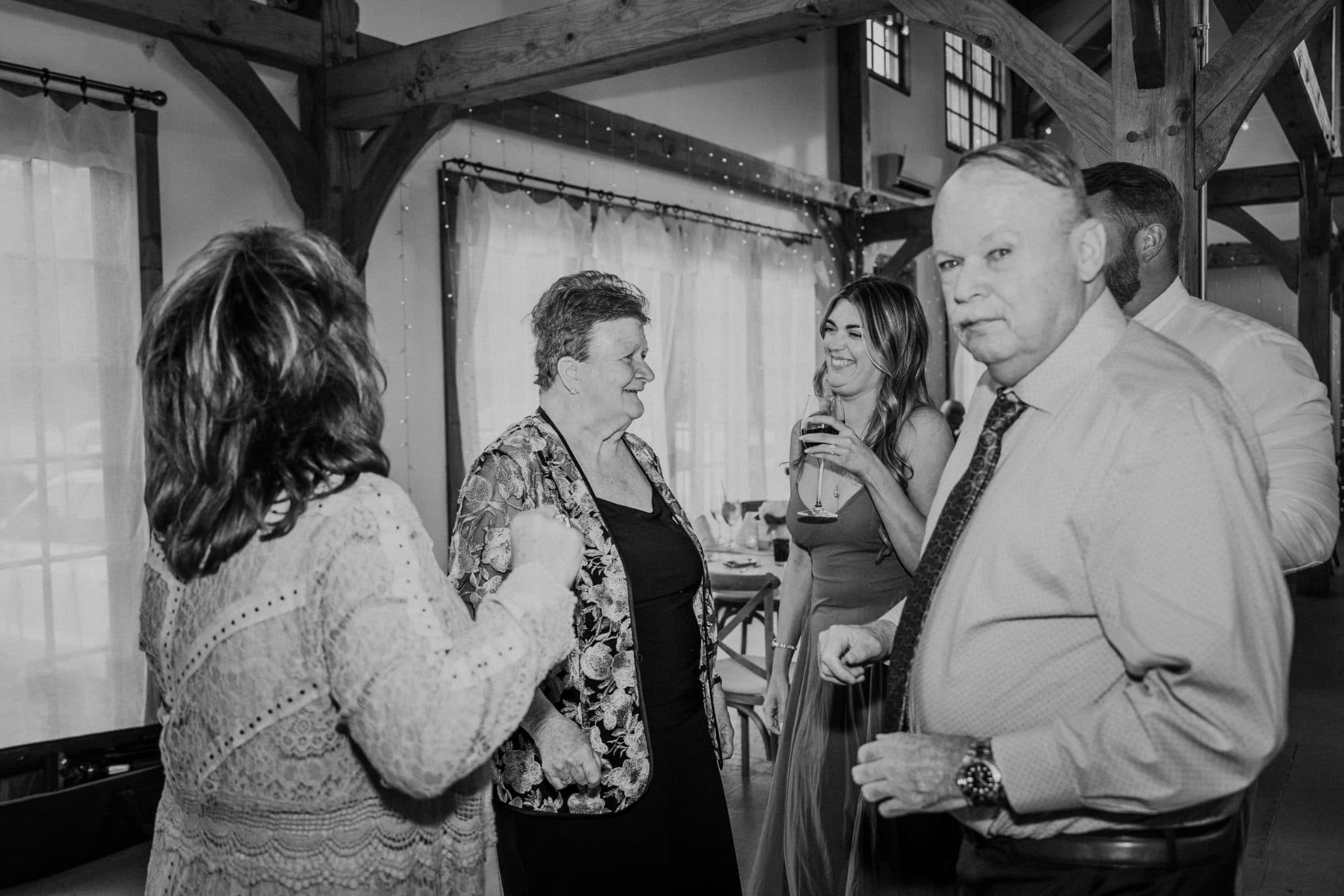 A group of people stands in a rustic room, engaged in conversation while holding drinks.