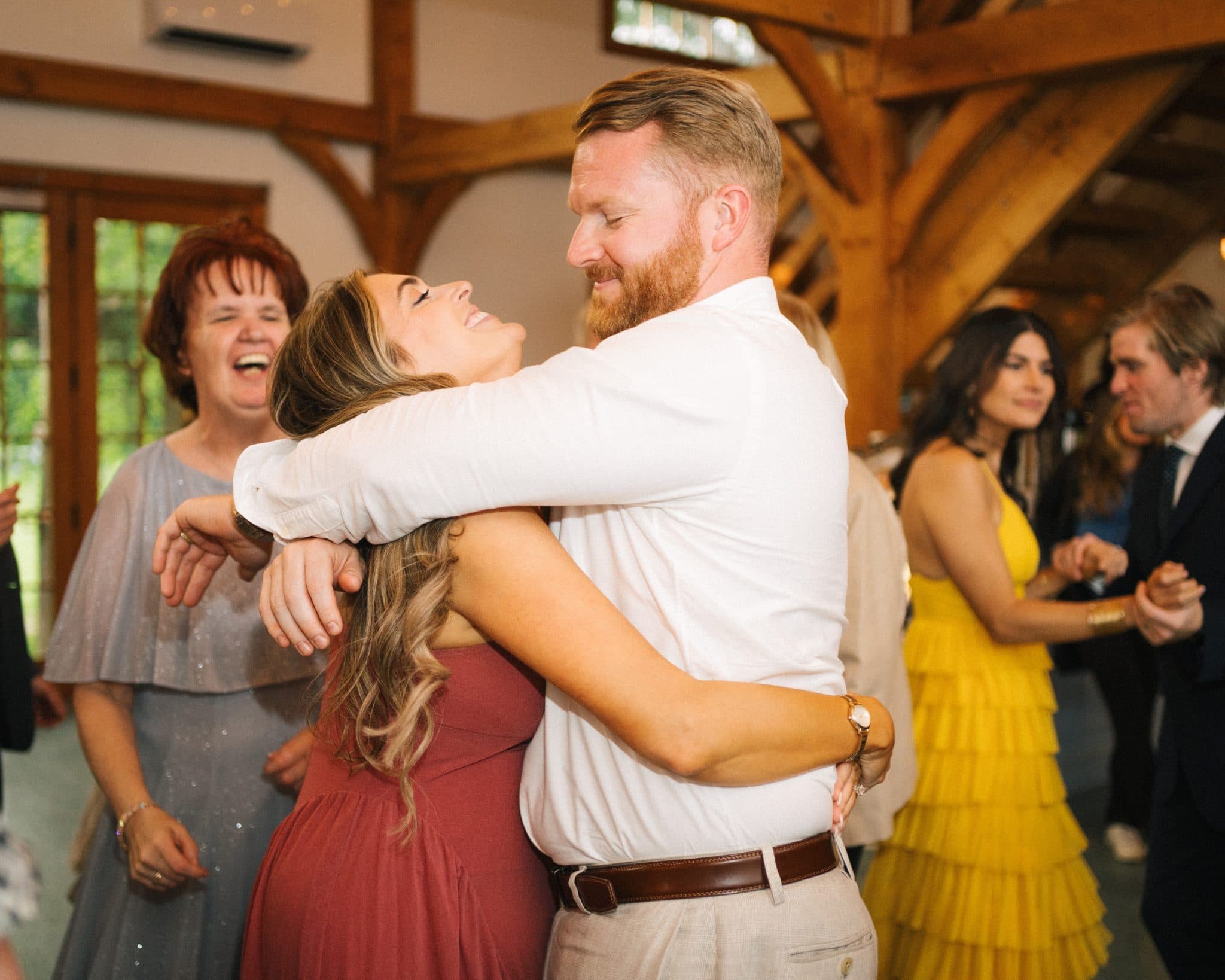A man in a white shirt hugs a woman in a red dress at a wedding reception.