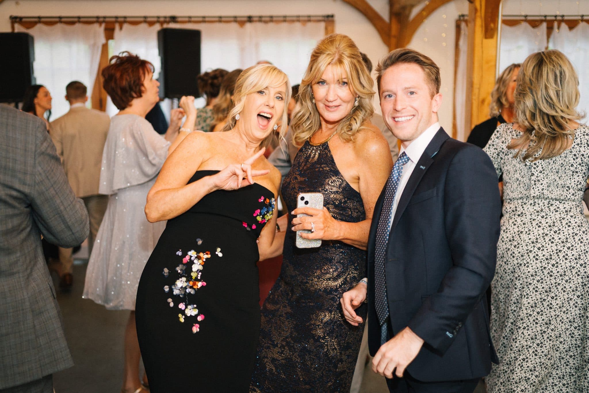 Three people pose for a photo at a wedding reception, smiling and holding a phone.