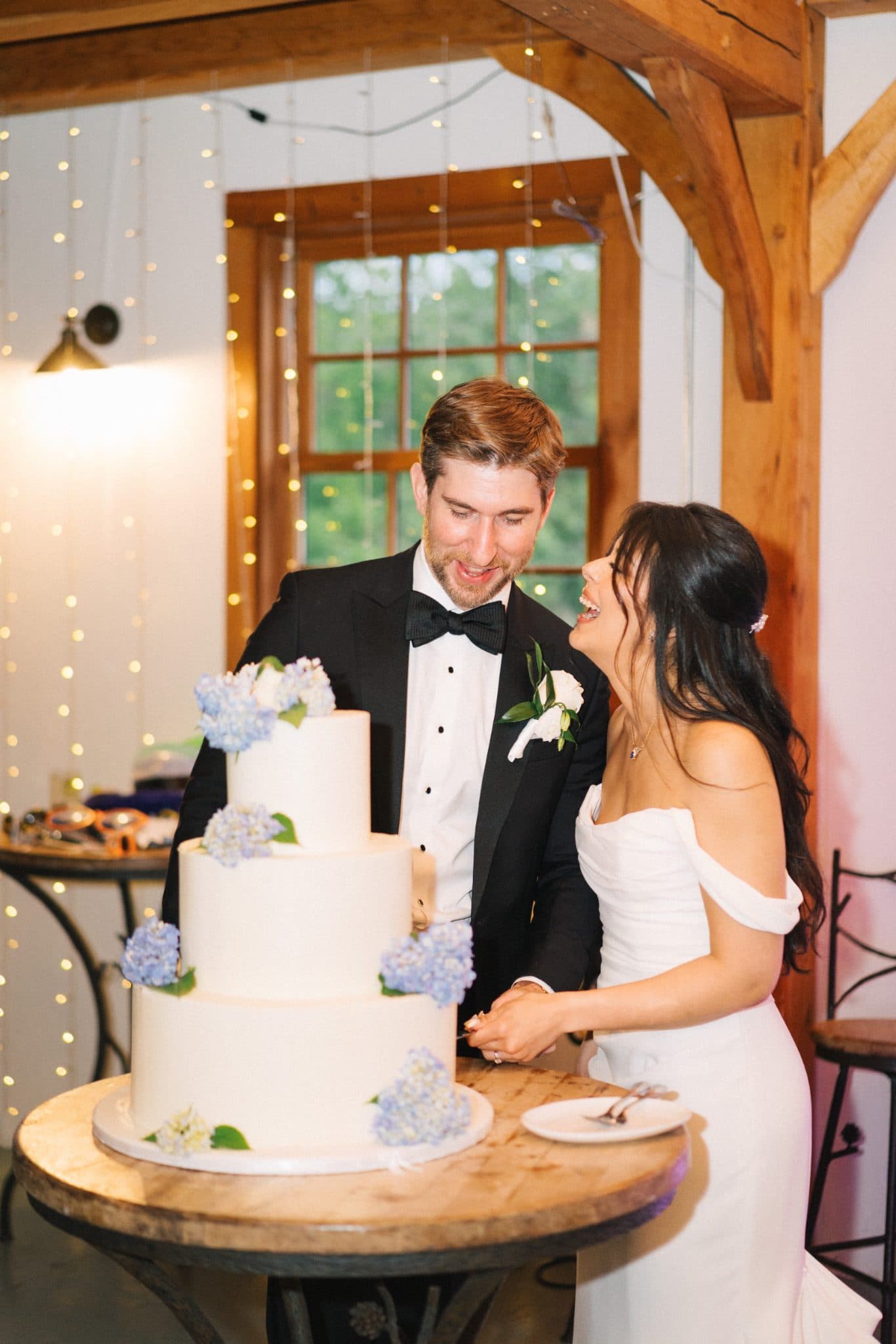 A bride and groom cut a three-tiered wedding cake decorated with blue hydrangeas.