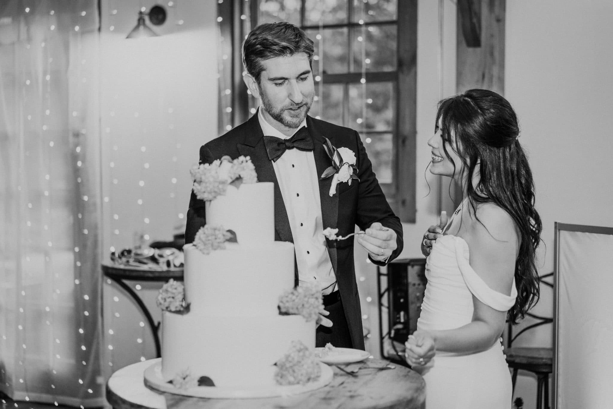 A bride and groom stand together, cutting a tiered wedding cake decorated with flowers.
