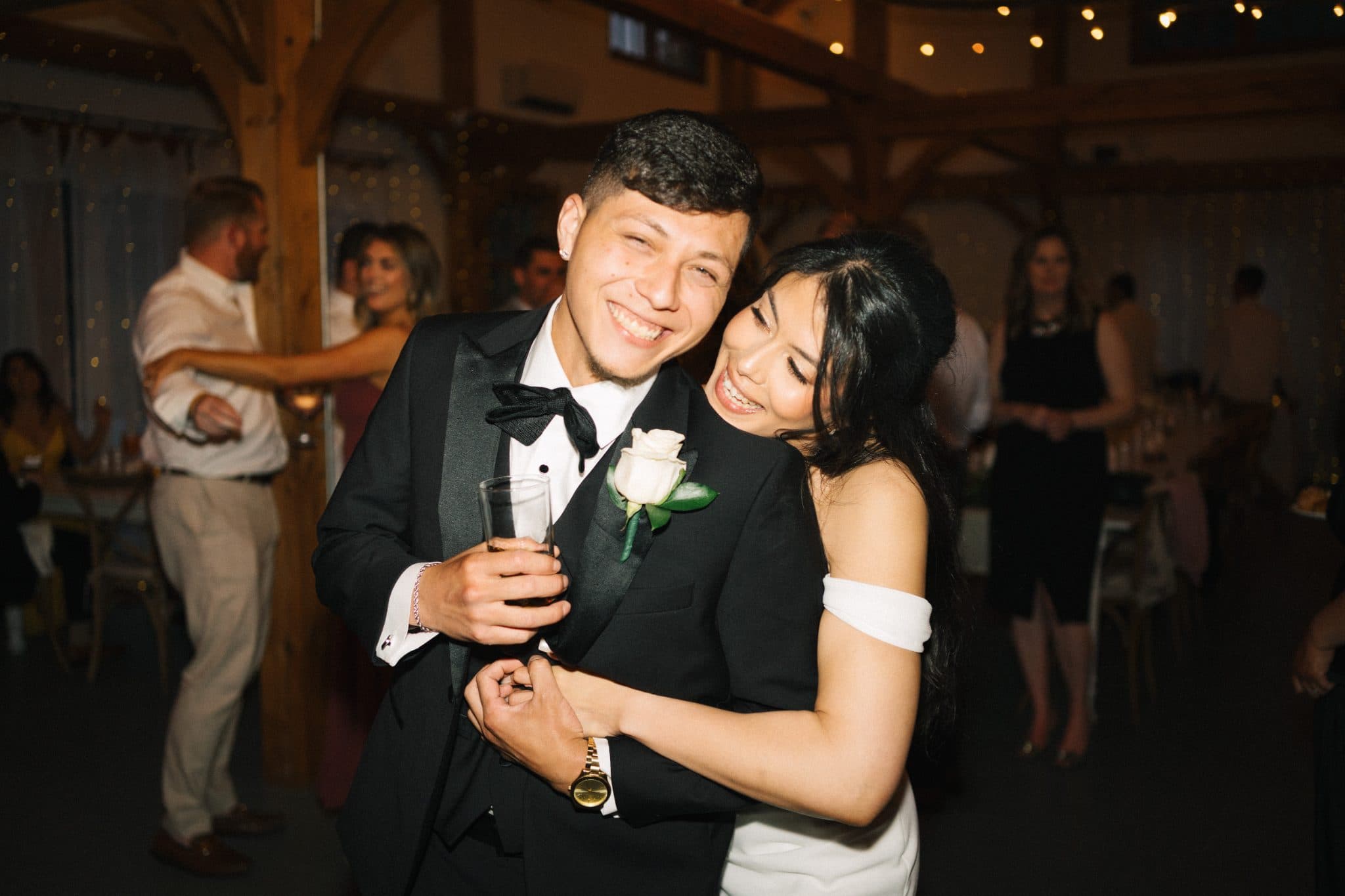 A couple in formal attire smiles and embraces at a wedding reception.